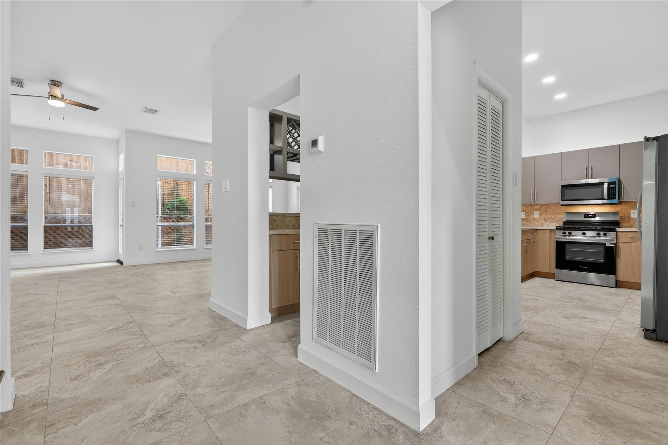 Bright and open-concept living area with high ceilings, large windows for natural light, tile flooring throughout, and seamless flow into the kitchen featuring stainless steel appliances, gas range, recessed lighting, and modern cabinetry. Neutral tones and spacious layout create the perfect setting for entertaining and everyday living. Bright and open-concept living area with high ceilings, large windows for natural light, tile flooring throughout, and seamless flow into the kitchen featuring stainless steel appliances, gas range, recessed lighting, and modern cabinetry. Neutral tones and spacious layout create the perfect setting for entertaining and everyday living.