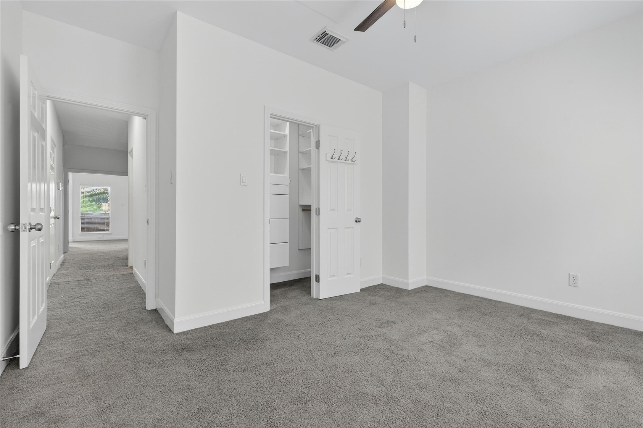 Spacious secondary bedroom featuring plush carpet, ceiling fan, neutral designer paint, and custom walk-in closet with built-in storage. Bright and versatile layout offers comfort and functionality, perfect for guests, family, or a home office setup.
