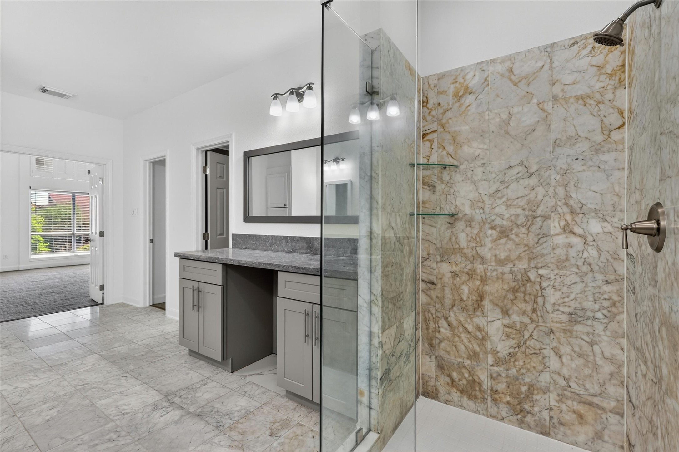 Spa-inspired primary bathroom featuring a frameless glass walk-in shower with designer marble-look tile, oversized vanity with granite countertops, modern cabinetry, and updated lighting. Bright open layout with luxury finishes creates a relaxing owners retreat buyers will love.