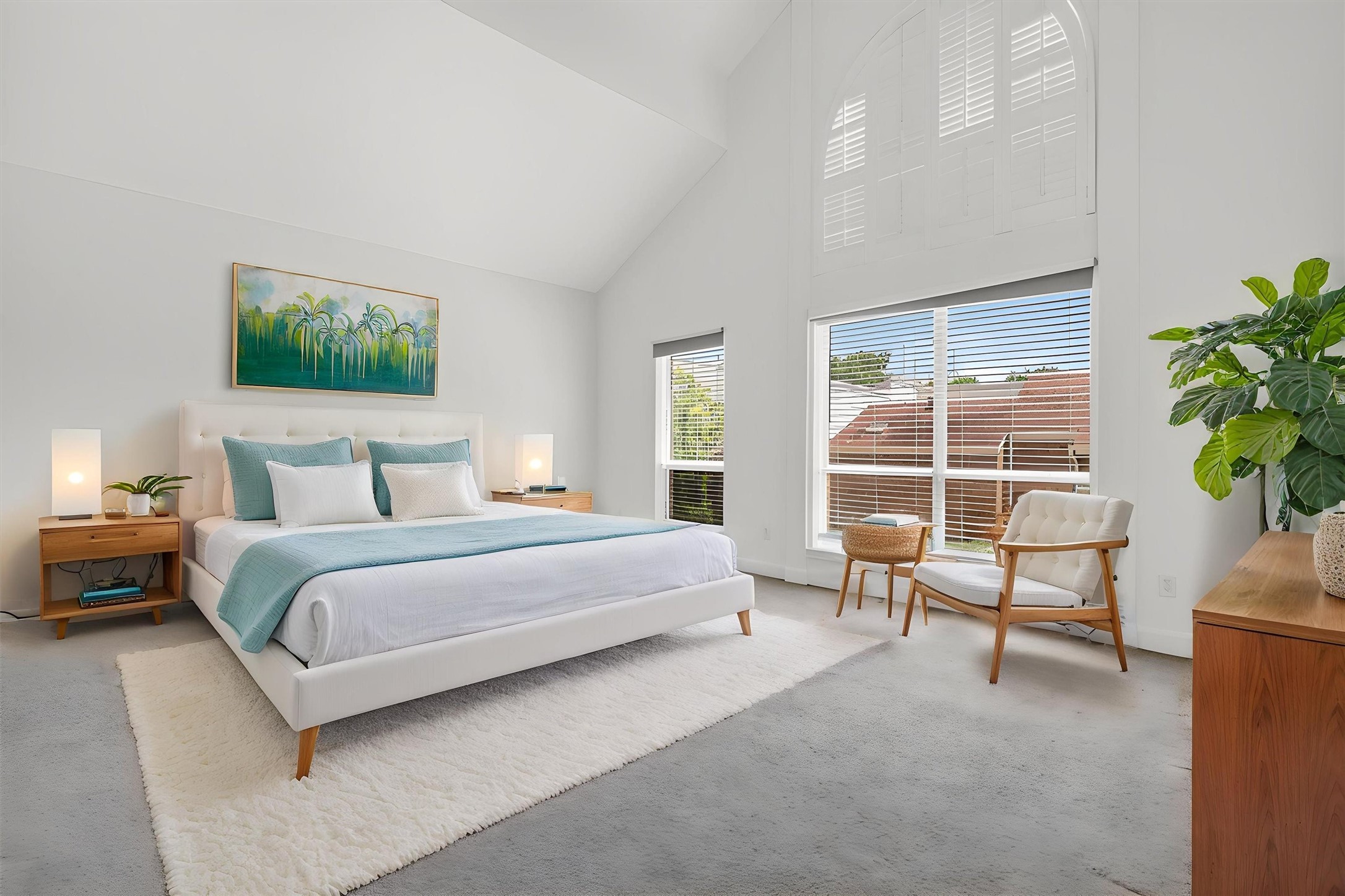**Virtually staged photo** of the spacious primary suite featuring soaring vaulted ceilings, oversized windows, abundant natural light, and plush carpet. Relaxing retreat offers an open layout with room for a sitting area, while large arched windows with plantation shutters create an elegant and airy feel buyers will love.