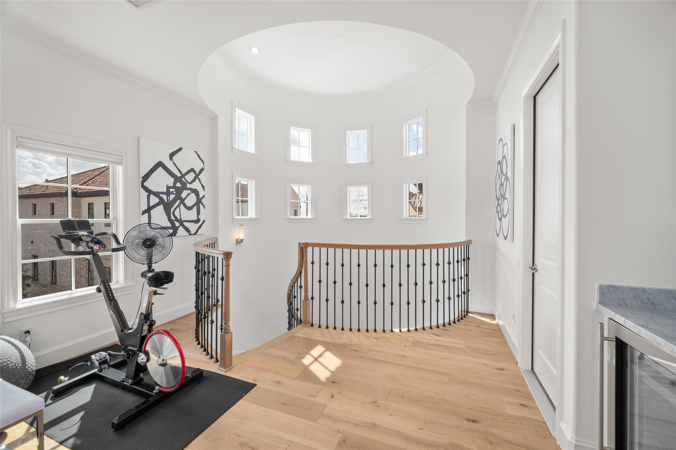 Light filled landing with soaring ceilings, curved staircase, beautiful hardwood floors, and an  abundance of windows.
