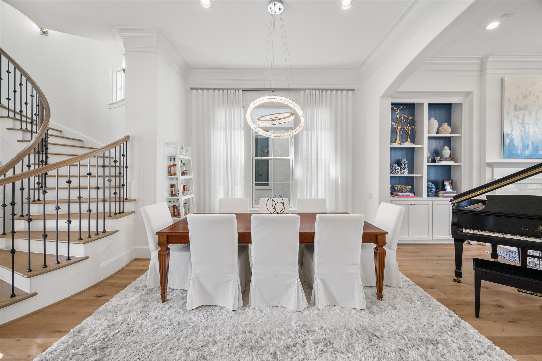 Formal dining room anchored by a sculptural ring chandelier, with wide-plank oak floors, tailored millwork, and custom built-ins beyond.