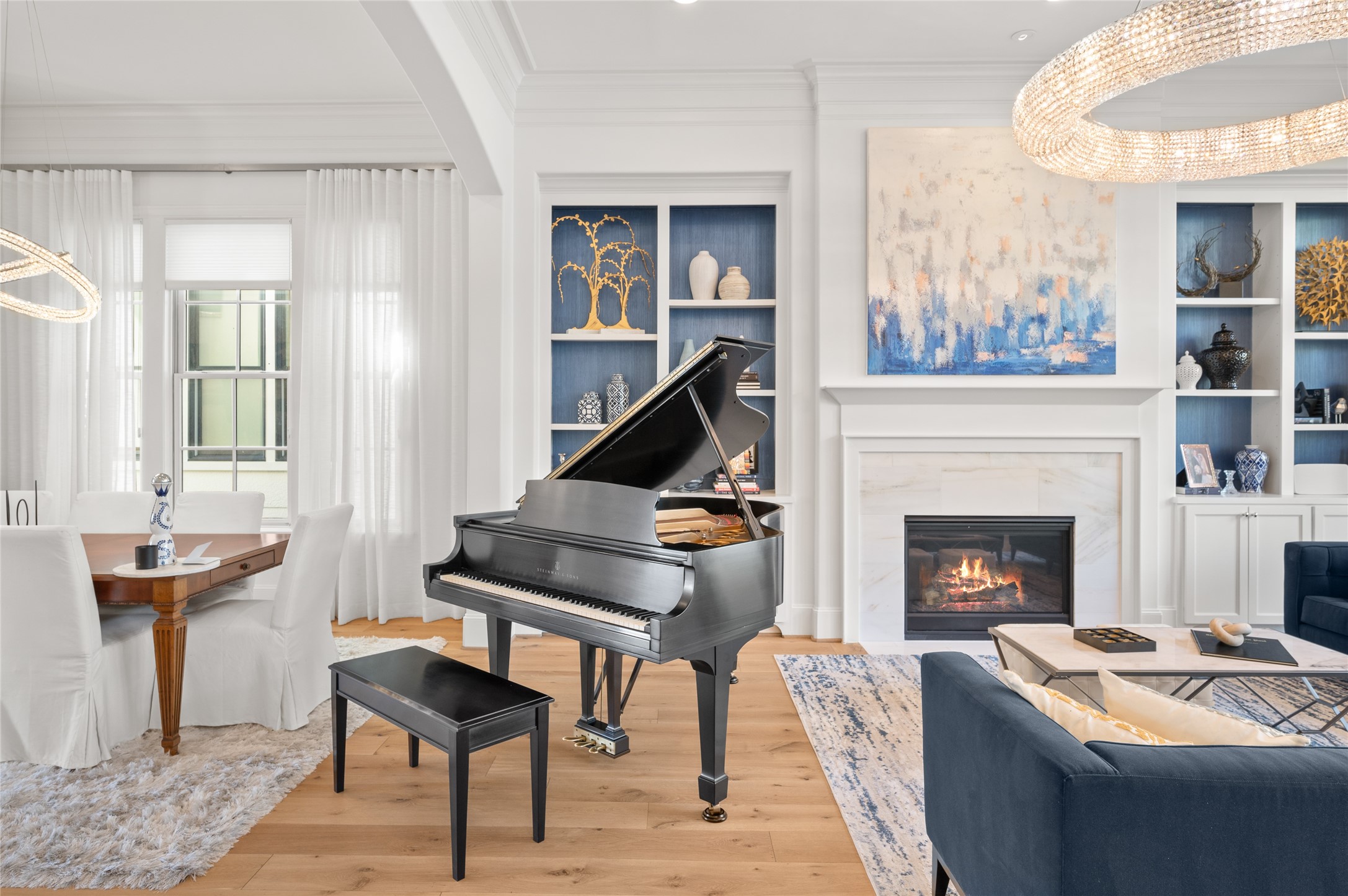 A striking Steinway grand piano complements the home's interconnected living and dining spaces, framed by custom blue-accented built-ins and a marble-surround fireplace.