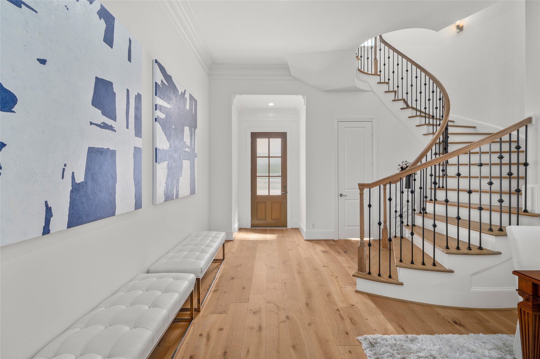 An elegant entryway featuring wide-plank hardwood floors, refined crown molding, and a sweeping curved staircase with wrought-iron balusters and natural wood accents.