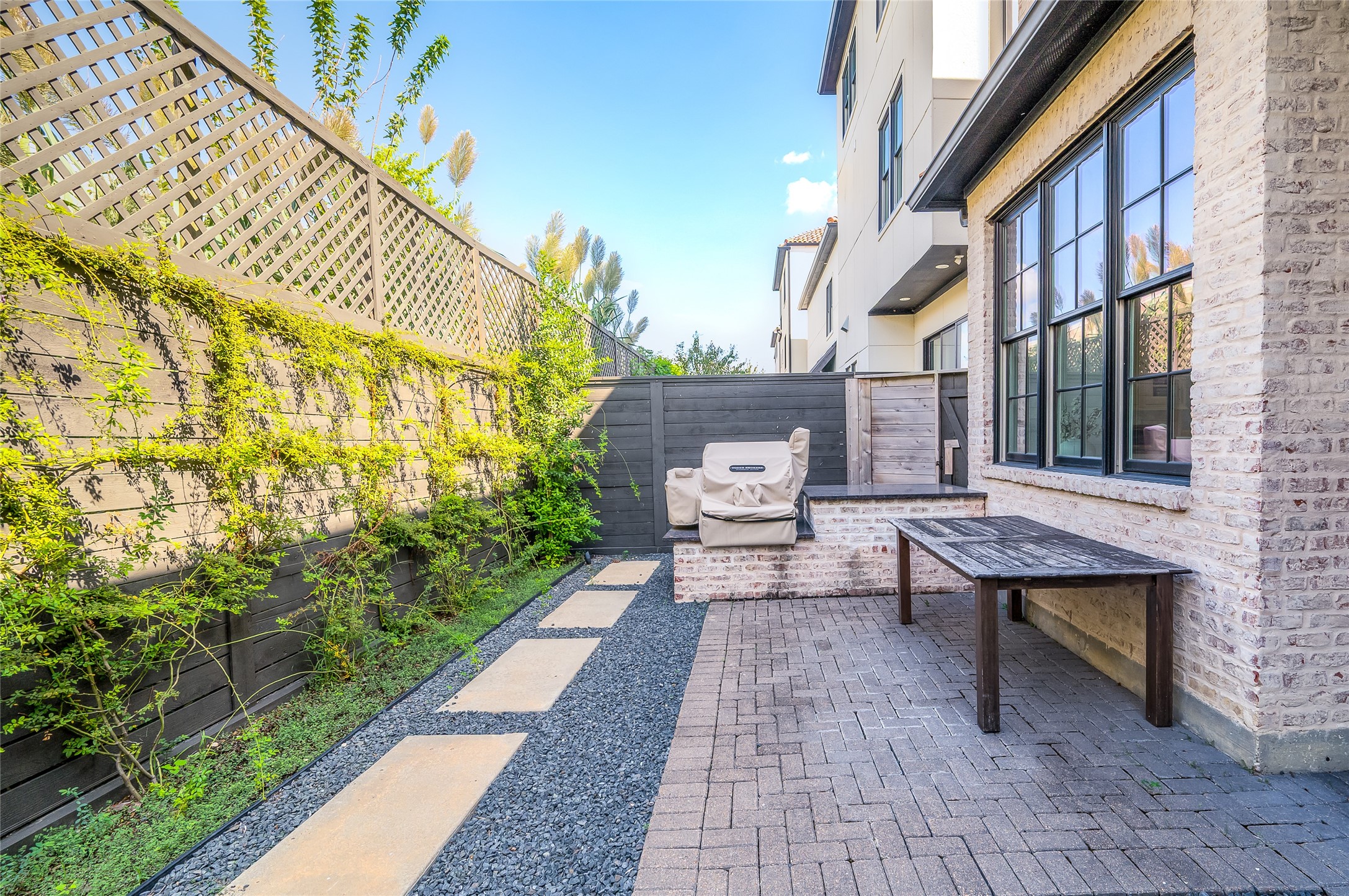 Outdoor retreat with French doors, brick-paved patio, landscaped borders, and a dedicated seating area creates a peaceful atmosphere.