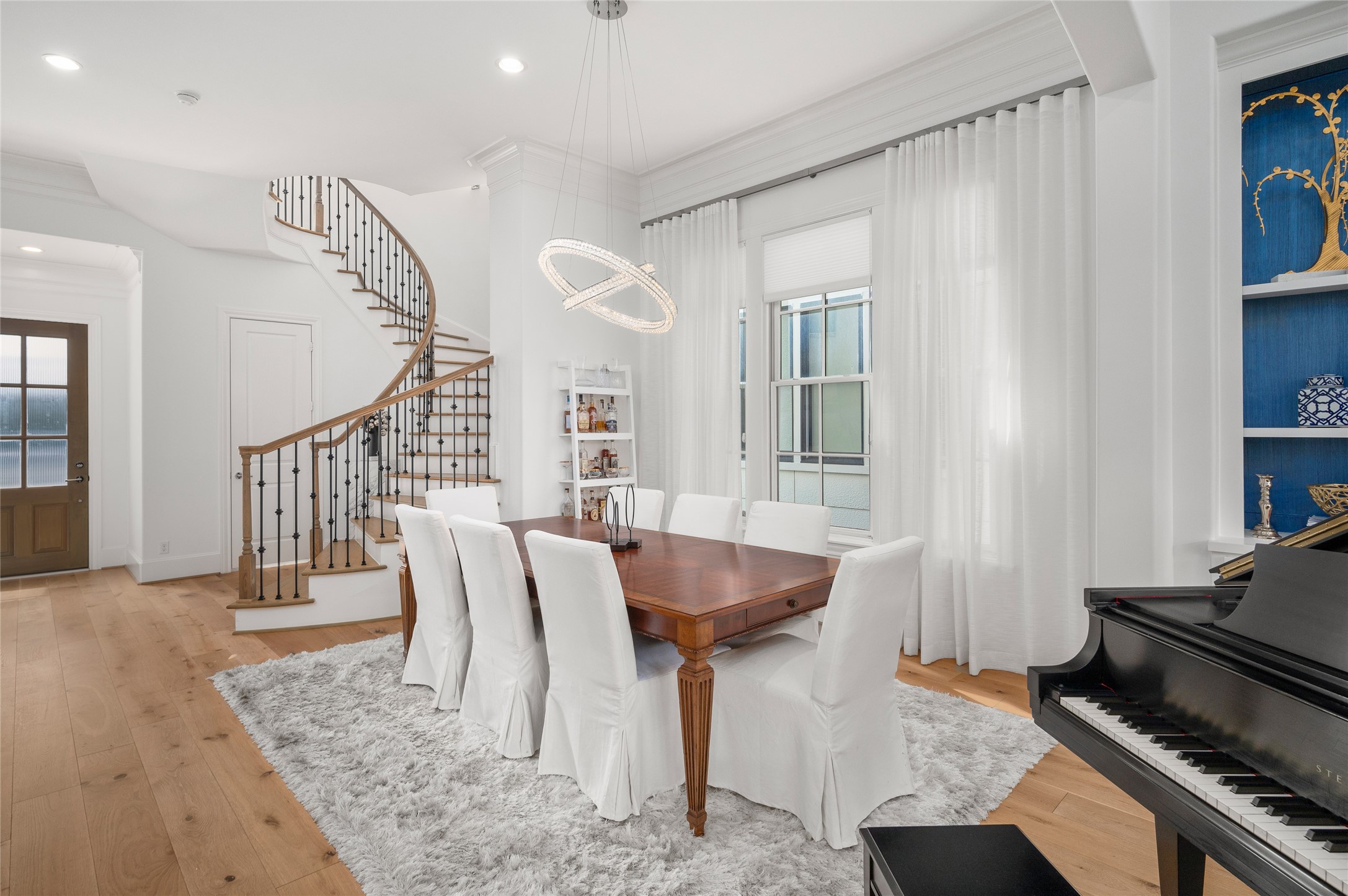 A second perspective captures the curved staircase with wrought-iron detailing and the dining room's understated architectural finishes.