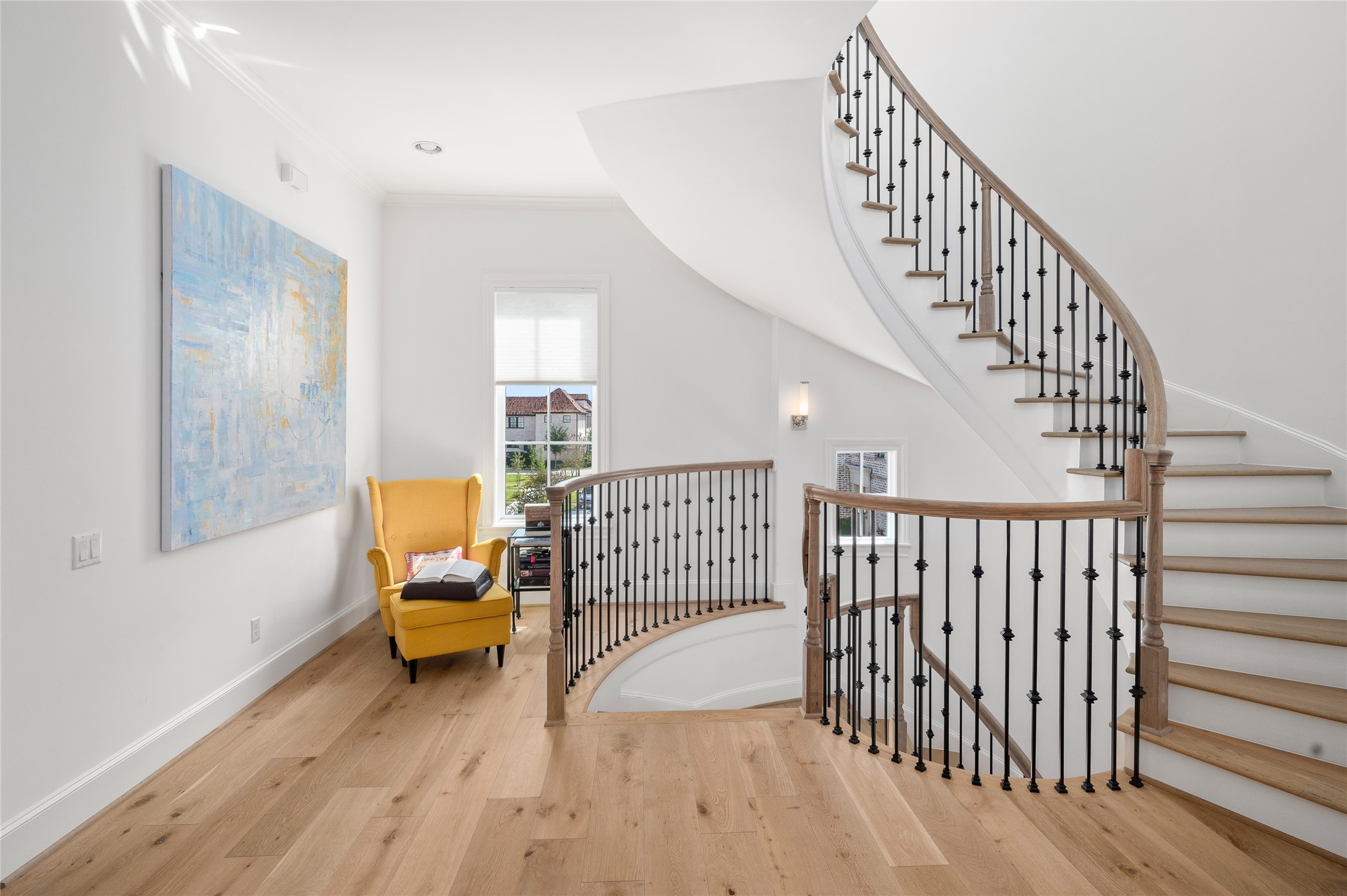 Architectural curved staircase with natural wood handrails, iron balusters, and an adjacent sitting nook.