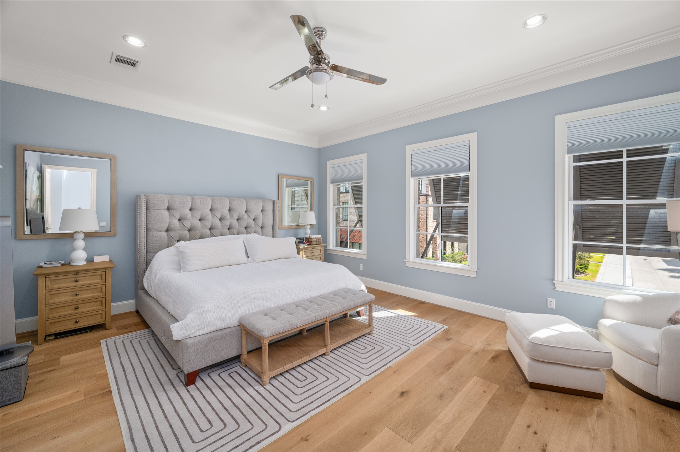 Generously proportioned primary bedroom suite with soft blue walls, wide-plank hardwood flooring, and multiple windows providing natural light.