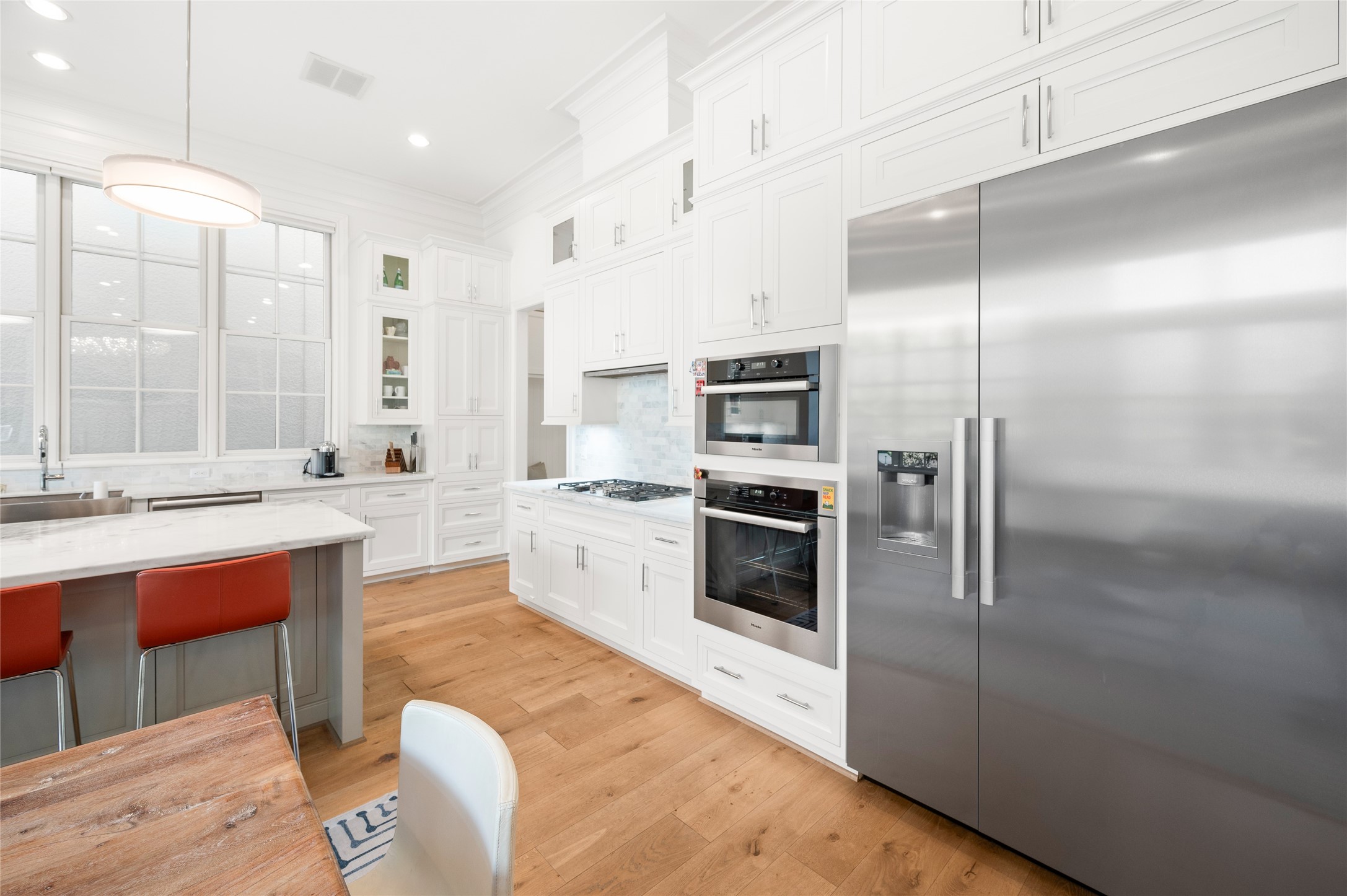 Miele steel appliances, including a built-in oven, microwave, gas cooktop, and French-door refrigerator, are set within floor-to-ceiling custom cabinetry.