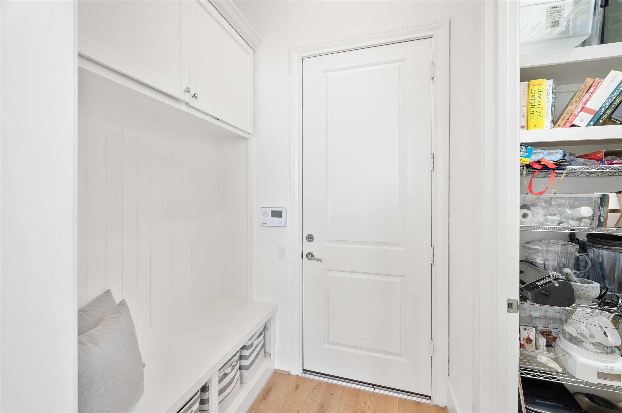 Practical mudroom with a built-in bench, overhead cabinetry, and convenient access to the walk-in pantry and the garage.