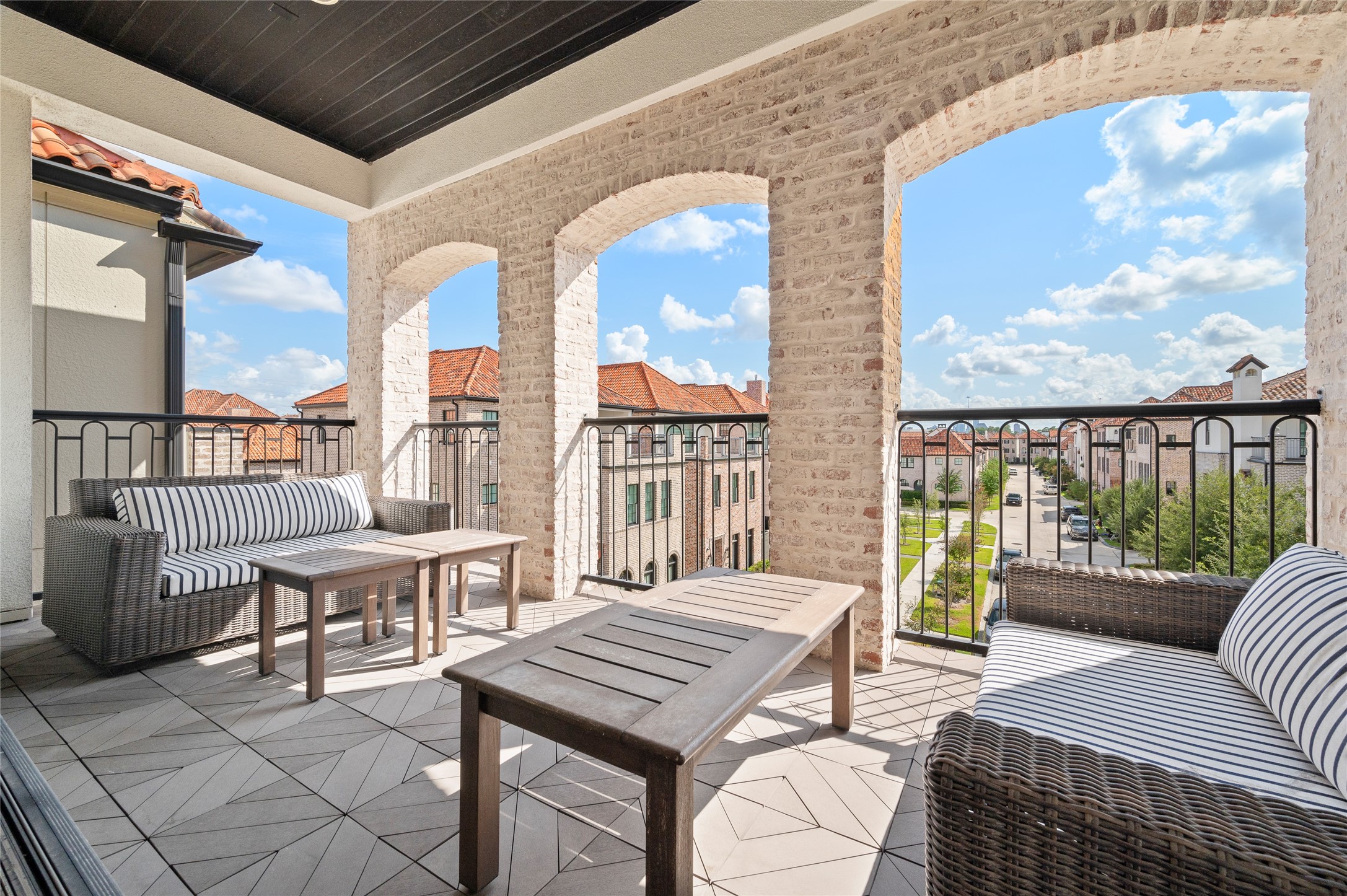Expansive covered balcony with charming brick archways, outdoor seating, and picturesque neighborhood views.