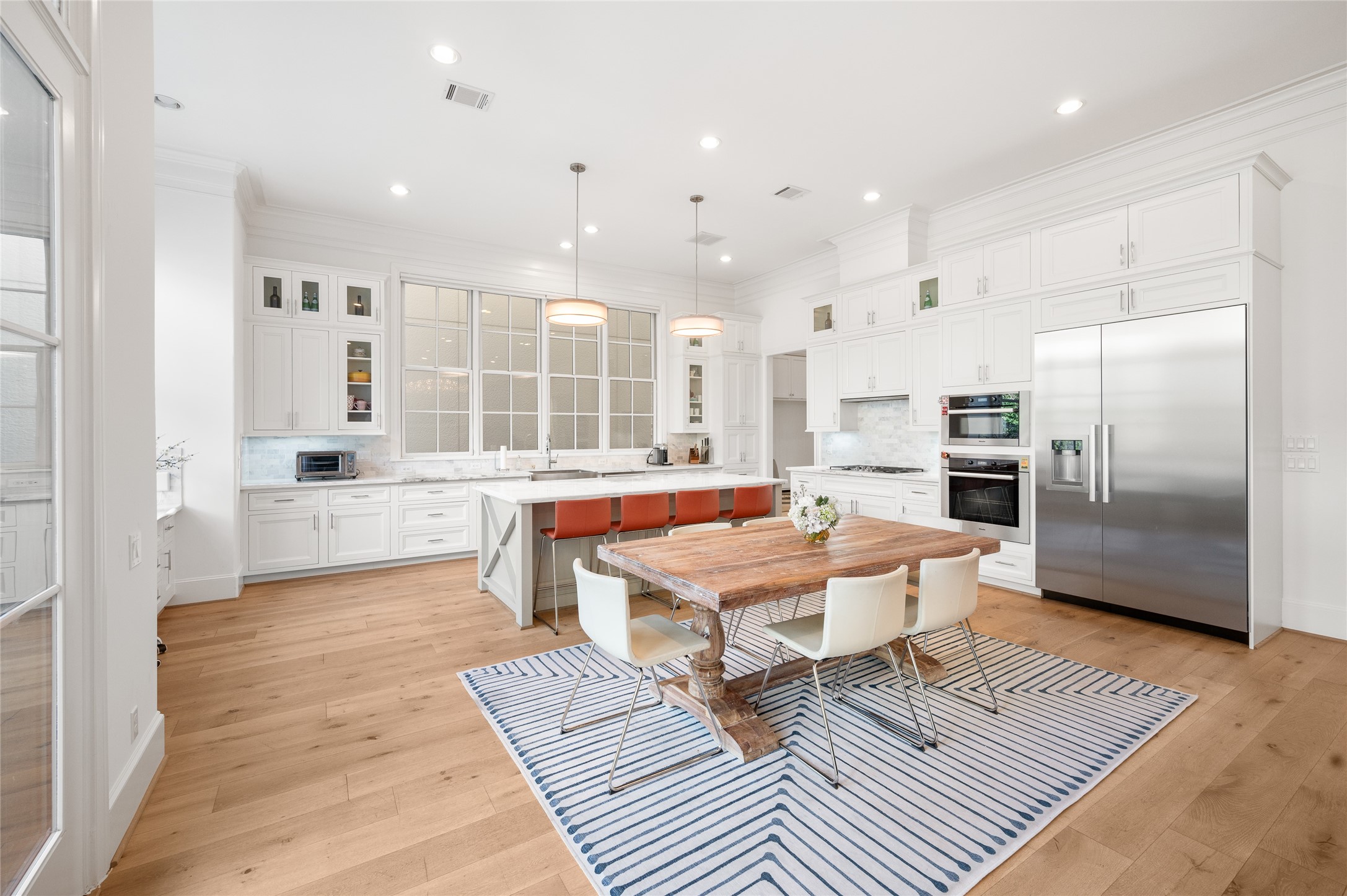 Generously proportioned kitchen with ceiling-height cabinetry, an oversized island, marble countertops, stainless steel appliances, and a dedicated breakfast area.