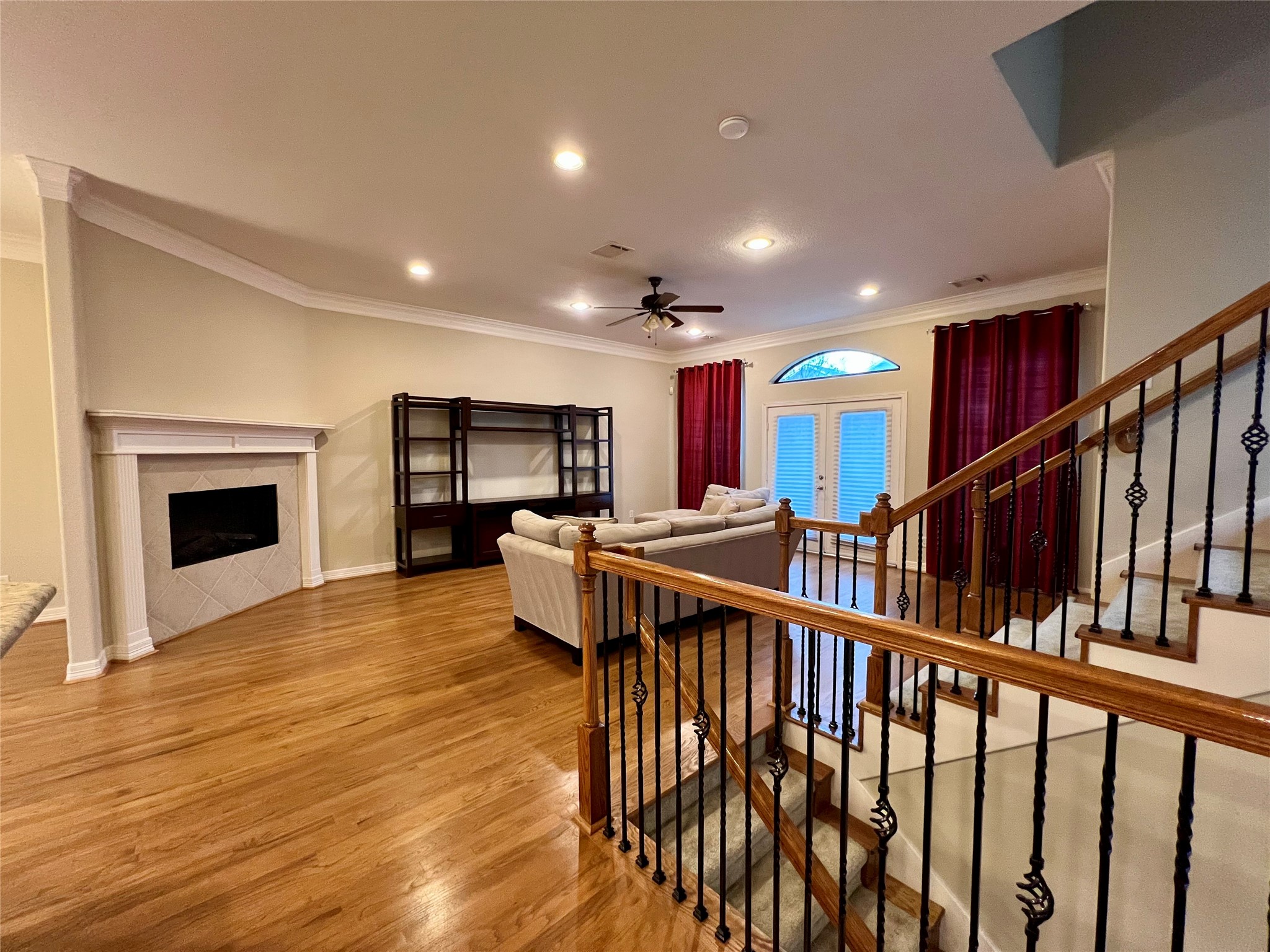 This spacious living room features hardwood flooring, a cozy fireplace, and ample natural light from large windows and glass doors. The room includes a built-in shelving unit and a comfortable seating area, with elegant iron and wood railing on the staircase for added style. This spacious living room features hardwood flooring, a cozy fireplace, and ample natural light from large windows and glass doors. The room includes a built-in shelving unit and a comfortable seating area, with elegant iron and wood railing on the staircase for added style.