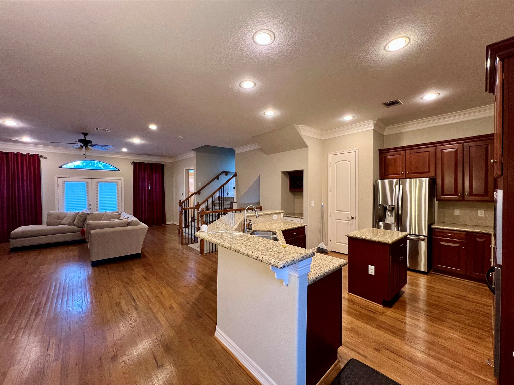 This open-concept living area features a spacious kitchen with granite countertops, stainless steel appliances, and rich wood cabinetry. The living room offers hardwood floors, a cozy sectional sofa, and ample natural light from large windows and glass doors. Perfect for entertaining and family living. This open-concept living area features a spacious kitchen with granite countertops, stainless steel appliances, and rich wood cabinetry. The living room offers hardwood floors, a cozy sectional sofa, and ample natural light from large windows and glass doors. Perfect for entertaining and family living.