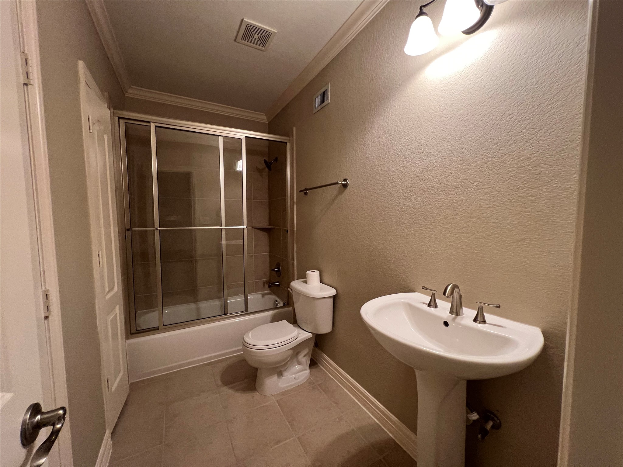 This bathroom features a bathtub with sliding glass doors, a pedestal sink, and a toilet. The neutral tile flooring and walls create a clean, modern look, complemented by overhead lighting. This bathroom features a bathtub with sliding glass doors, a pedestal sink, and a toilet. The neutral tile flooring and walls create a clean, modern look, complemented by overhead lighting.
