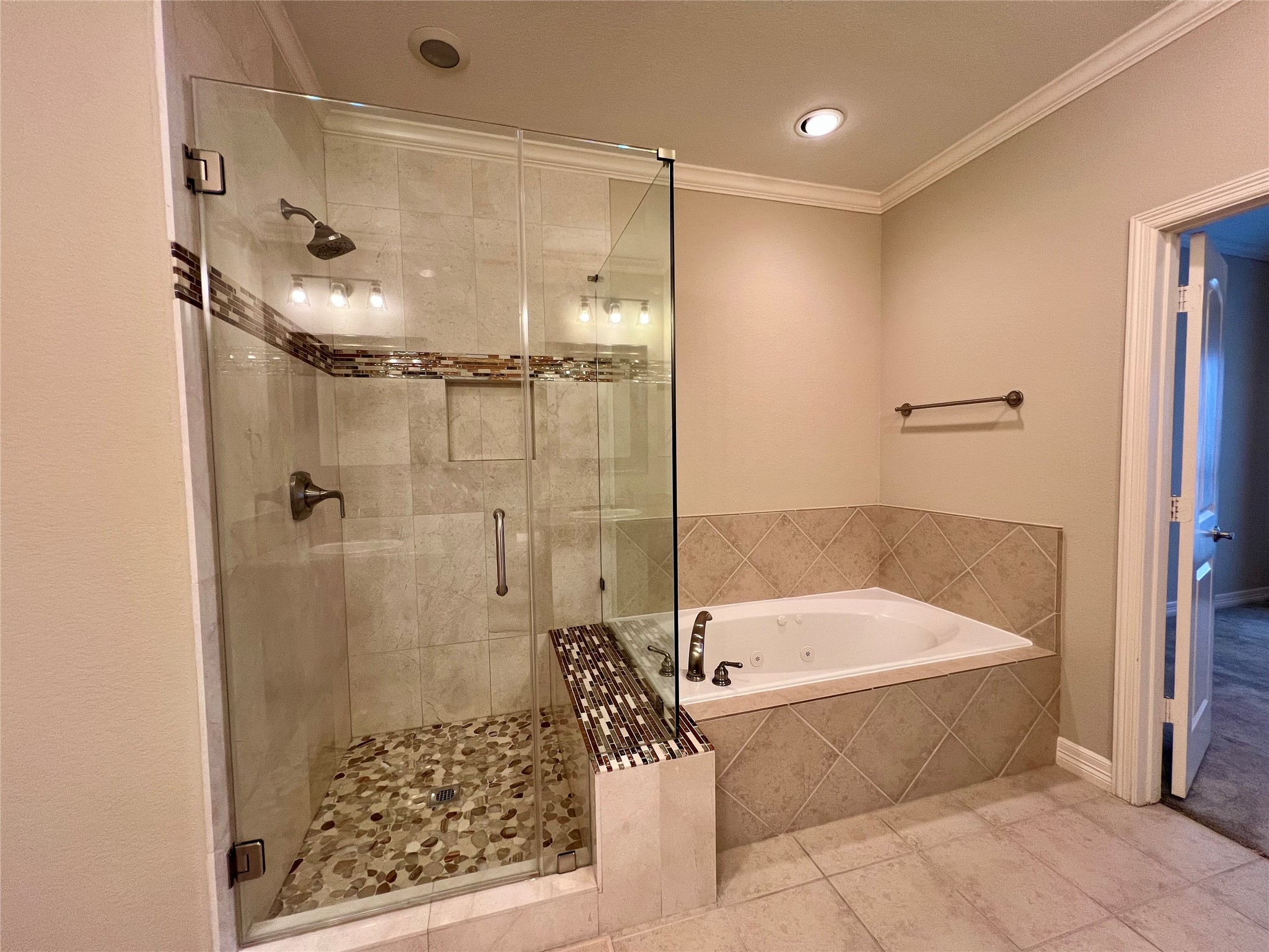 A modern glass-enclosed shower with stylish tilework and a separate built-in bathtub. The neutral tones and recessed lighting create a relaxing atmosphere.