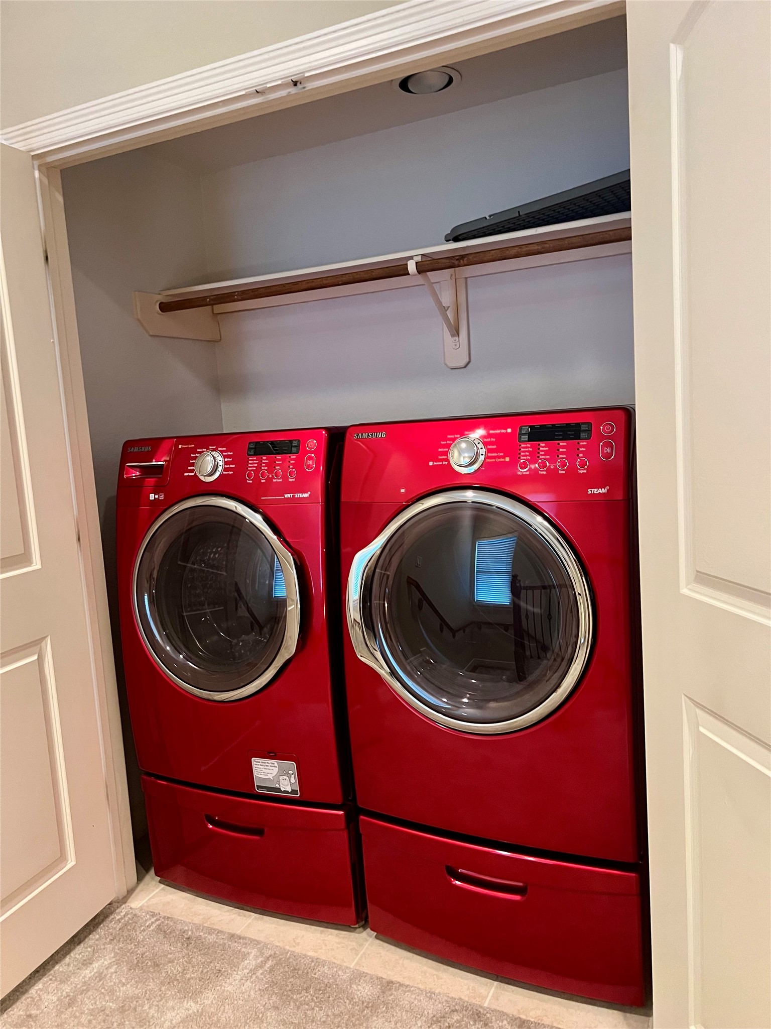 A laundry closet with a vibrant red front-loading washer and dryer set. There's a shelf above for storage, and the area is neatly enclosed by doors.