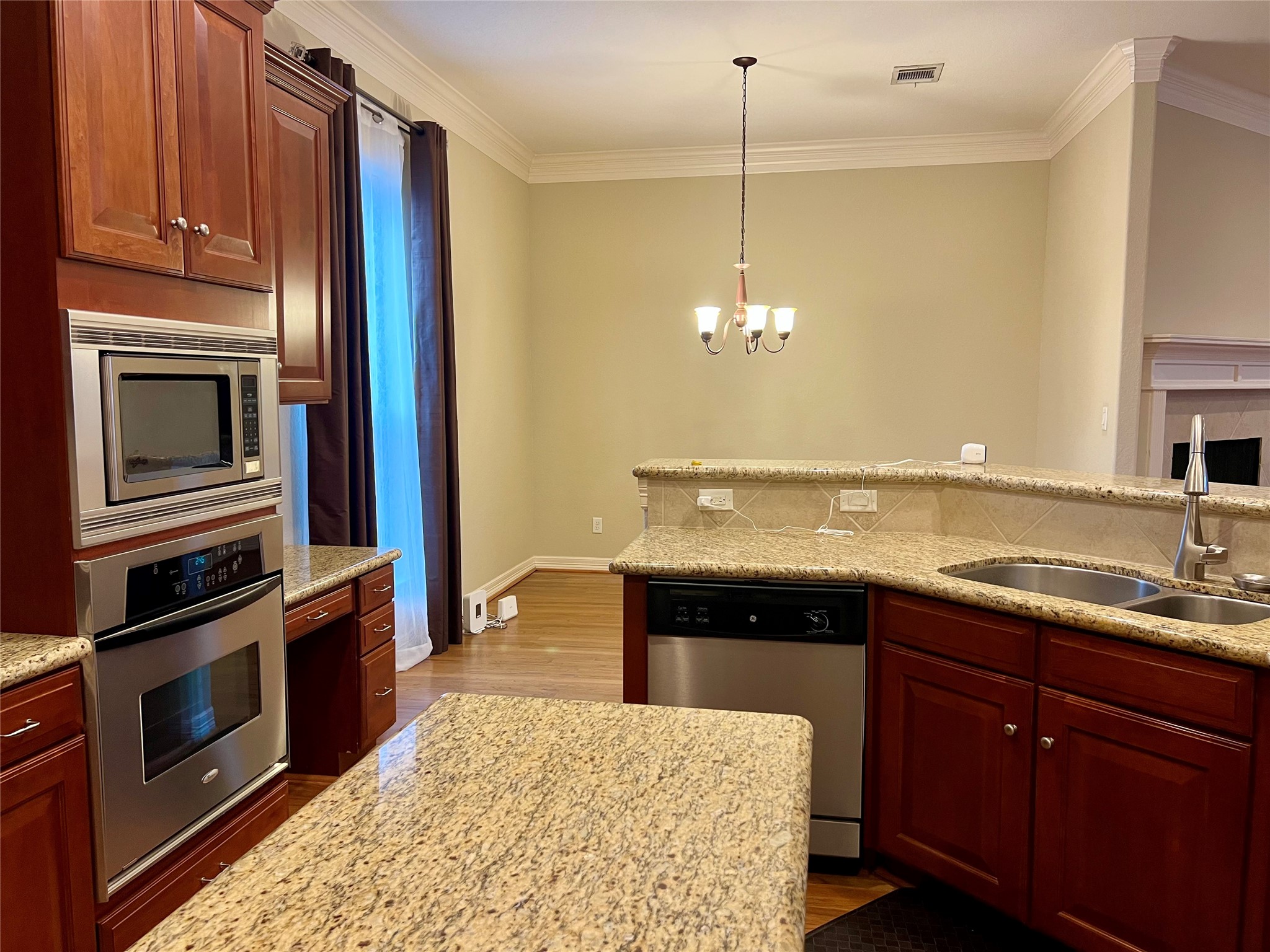 This kitchen features elegant granite countertops, stainless steel appliances, and rich wooden cabinetry. Its open layout, with a bar counter, overlooks a cozy dining area, enhanced by a stylish chandelier.