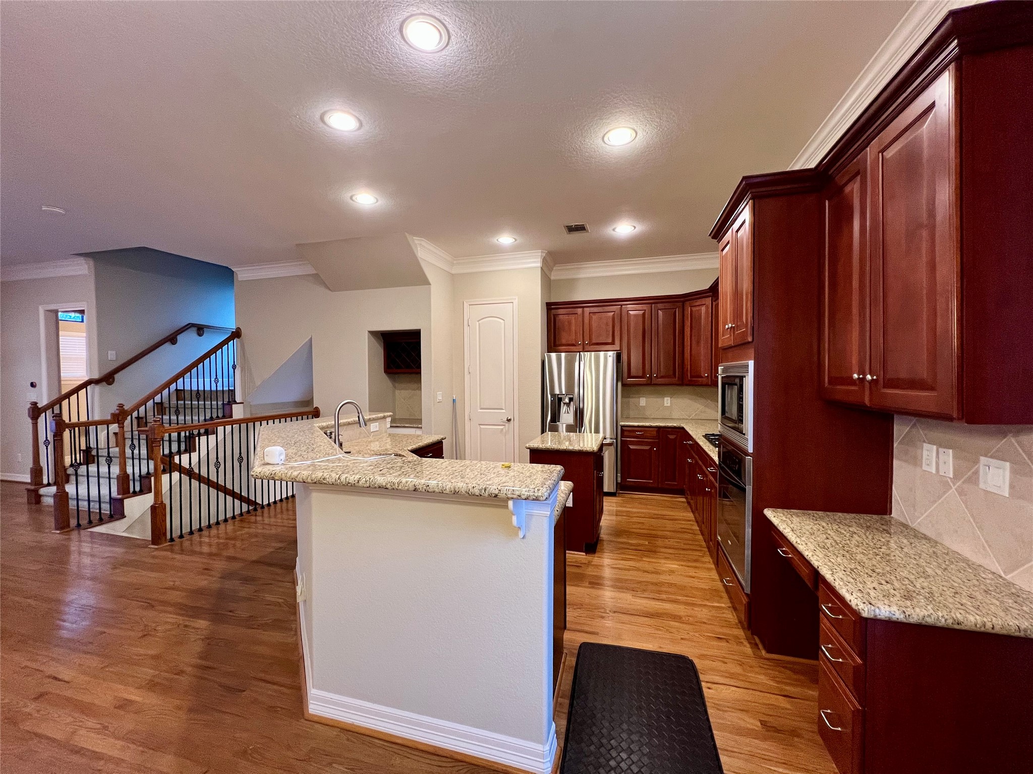 A spacious kitchen with rich wooden cabinets, granite countertops, and stainless steel appliances. The open layout connects to a staircase with elegant wooden railings, enhancing the home's warmth and functionality. A spacious kitchen with rich wooden cabinets, granite countertops, and stainless steel appliances. The open layout connects to a staircase with elegant wooden railings, enhancing the home's warmth and functionality.