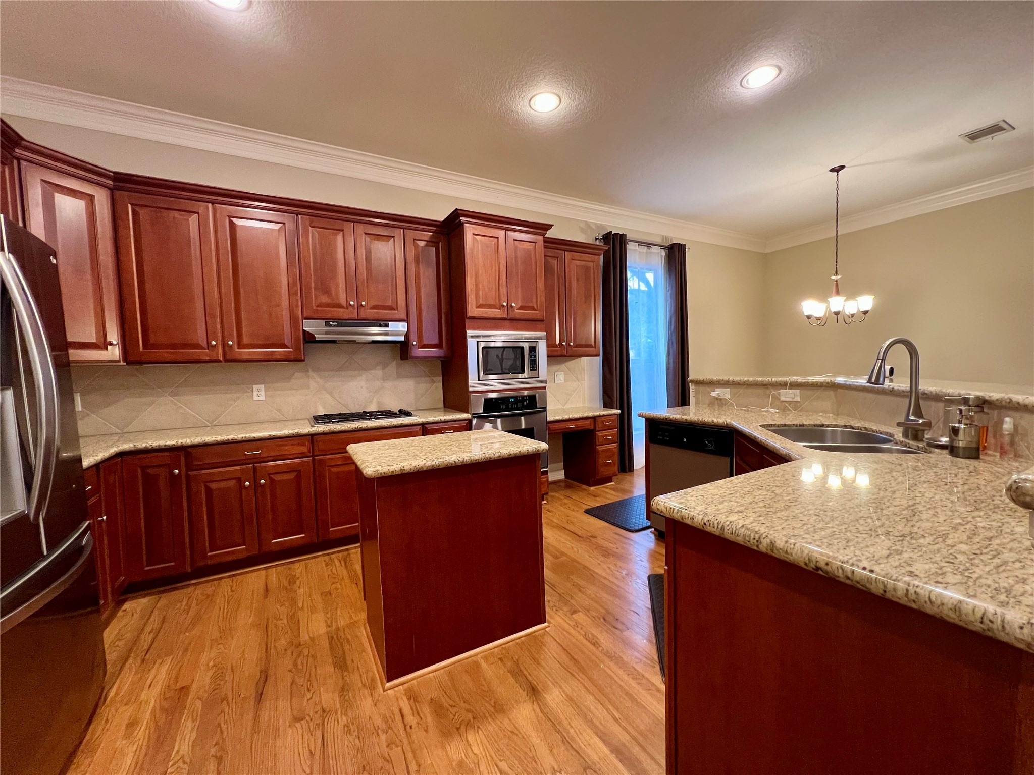 This kitchen features rich wood cabinetry, granite countertops, and hardwood floors. It includes stainless steel appliances, an island, and a modern light fixture, creating a warm and functional cooking space. This kitchen features rich wood cabinetry, granite countertops, and hardwood floors. It includes stainless steel appliances, an island, and a modern light fixture, creating a warm and functional cooking space.