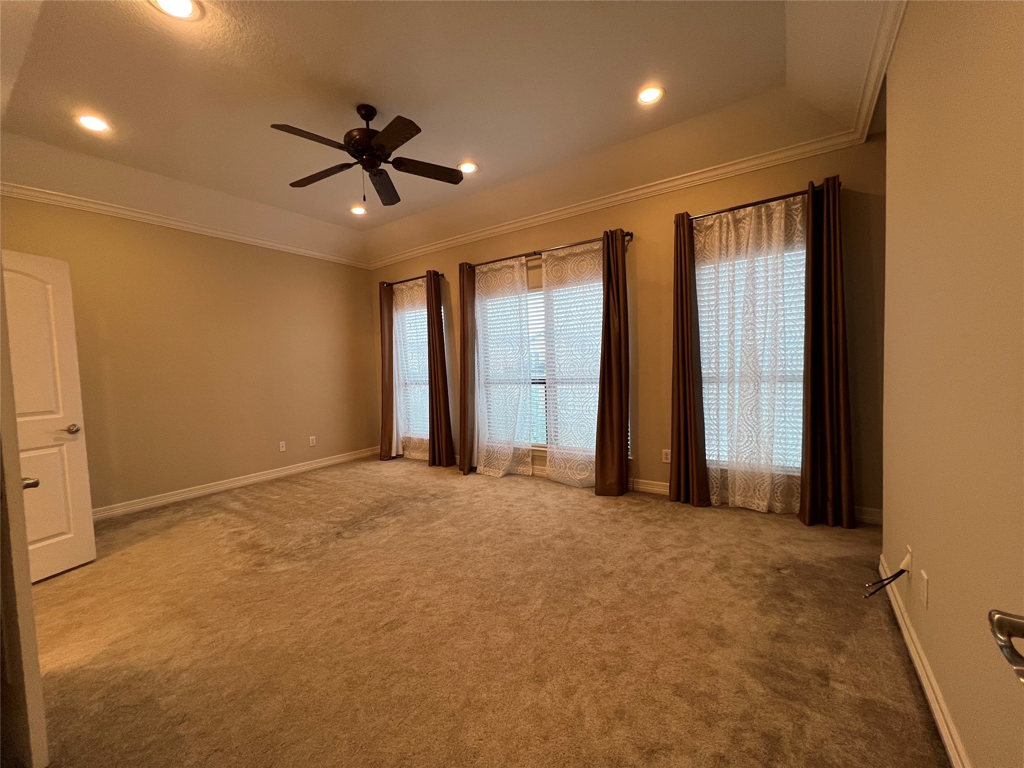 The master bedroom features neutral walls, plush carpeting, and large windows with curtains, allowing plenty of natural light. It includes recessed lighting and a ceiling fan, offering a comfortable and inviting atmosphere.