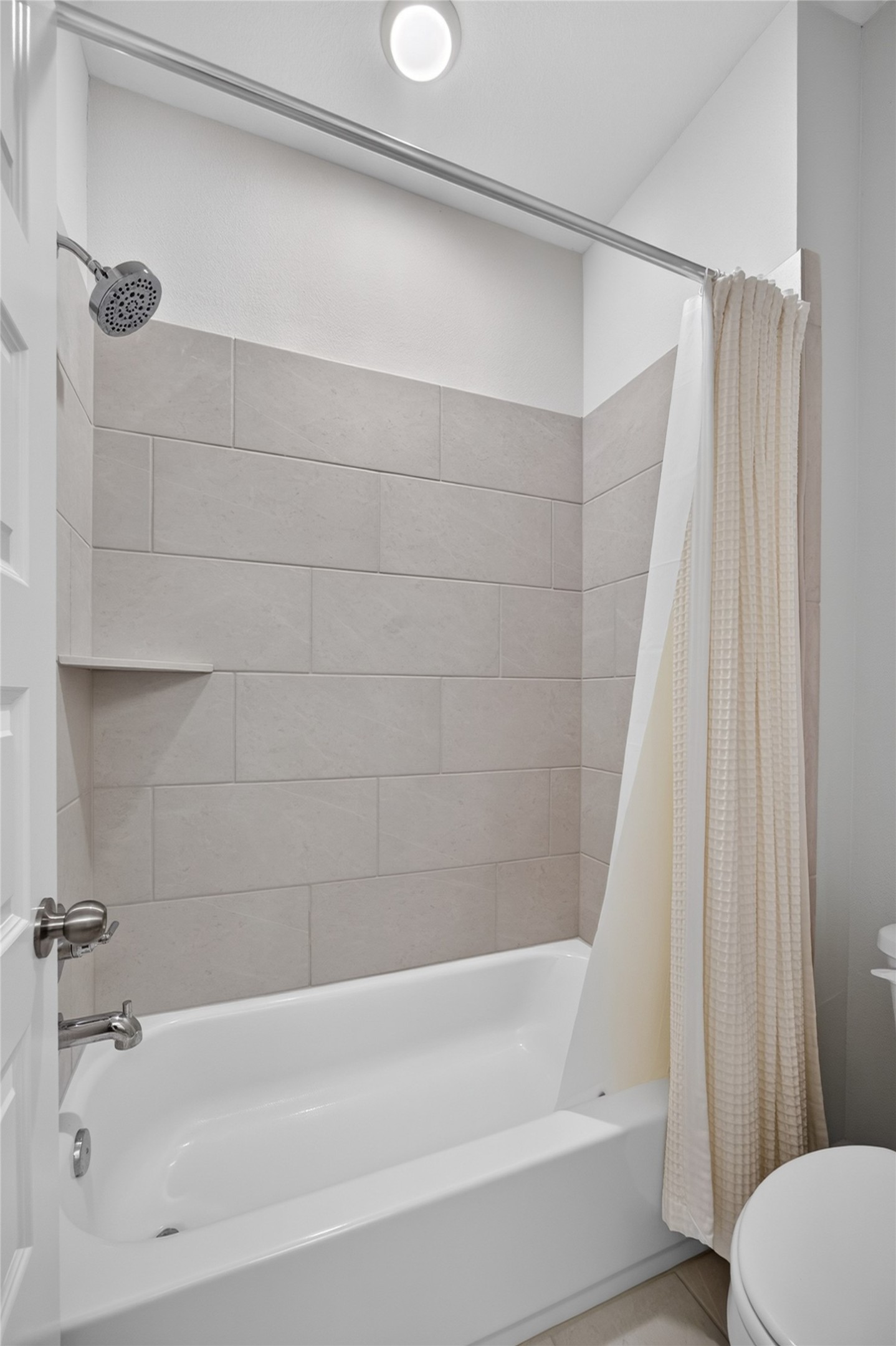 The secondary bathing area features a tub-and-shower combination with a large-format tile surround. A recessed niche keeps bathing essentials within reach, while the shower curtain allows the tub area to be easily enclosed. Neutral tile offers a versatile backdrop for a variety of decorative accents.