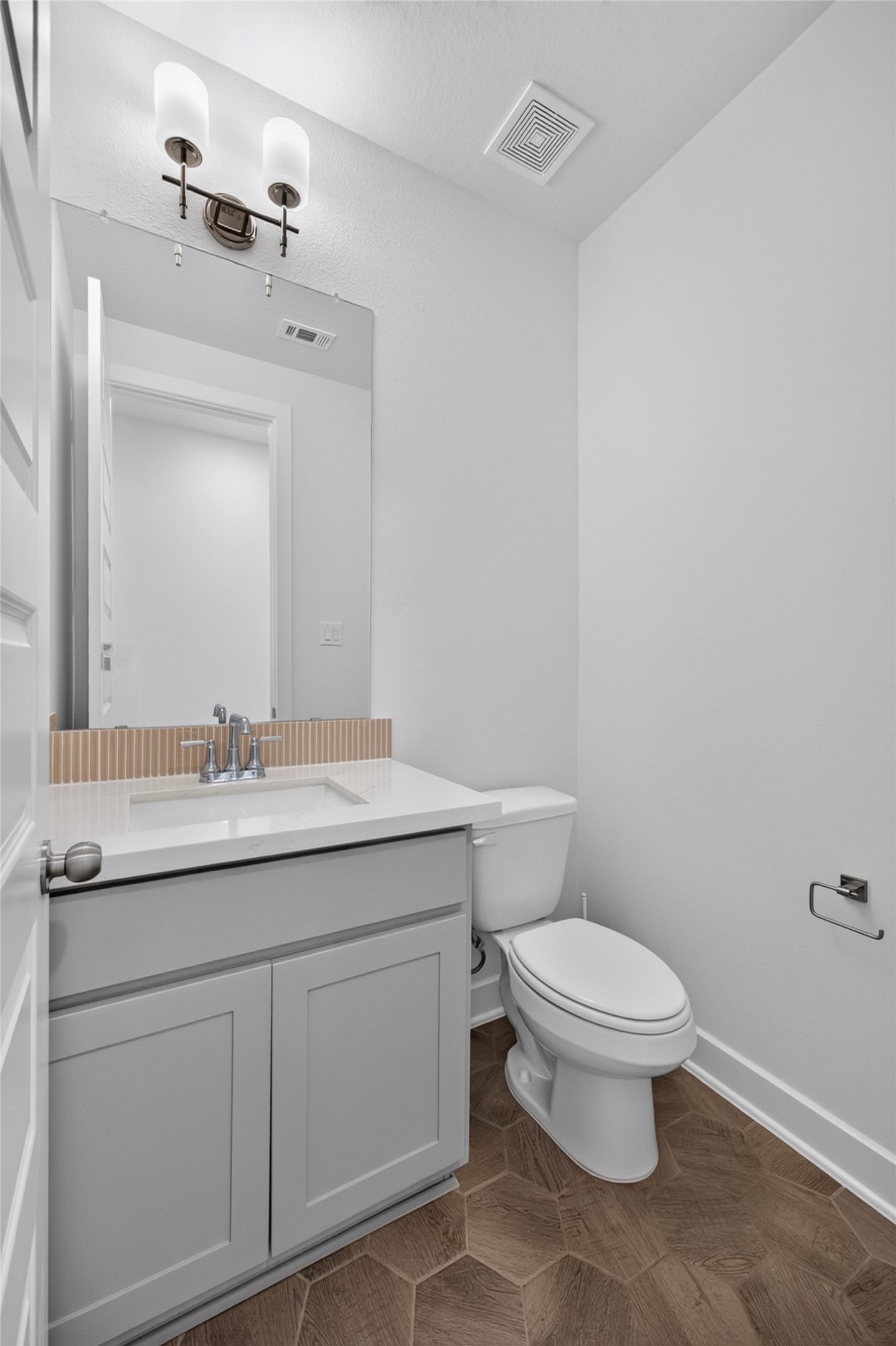 The first-floor powder room offers a convenient option for guests near the main living areas. A gray vanity pairs with a light countertop and chrome fixtures, while the large mirror enhances the sense of space. Cabinet storage keeps everyday essentials neatly tucked away.