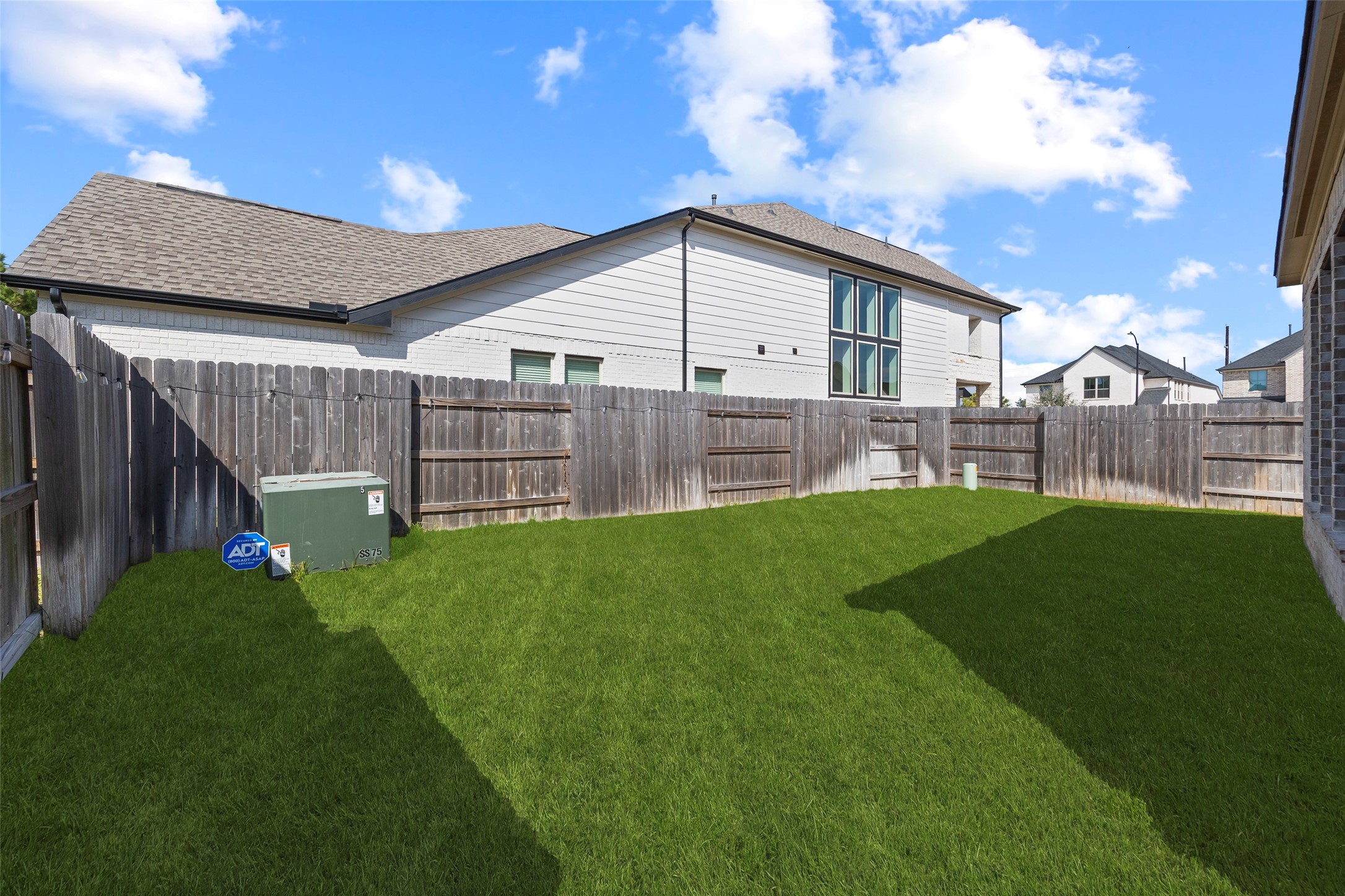 The backyard features an open stretch of lawn enclosed by wood privacy fencing. The grassy area offers flexibility for outdoor activities, garden beds or an additional seating arrangement. This view from near the covered patio shows the yards layout and the space available to personalize the outdoor setting.