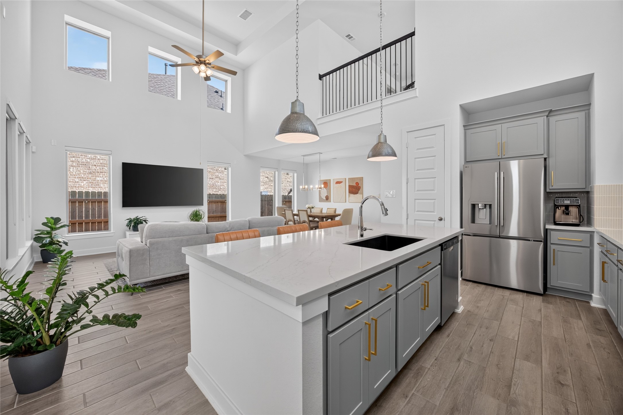 The kitchen features gray cabinetry, contrasting gold-tone hardware and light countertops surrounding a spacious center island. Pendant lights illuminate the islands workspace and seating area, while stainless steel appliances complement the finishes. Open sightlines into the family and dining rooms keep the kitchen connected to daily activities.