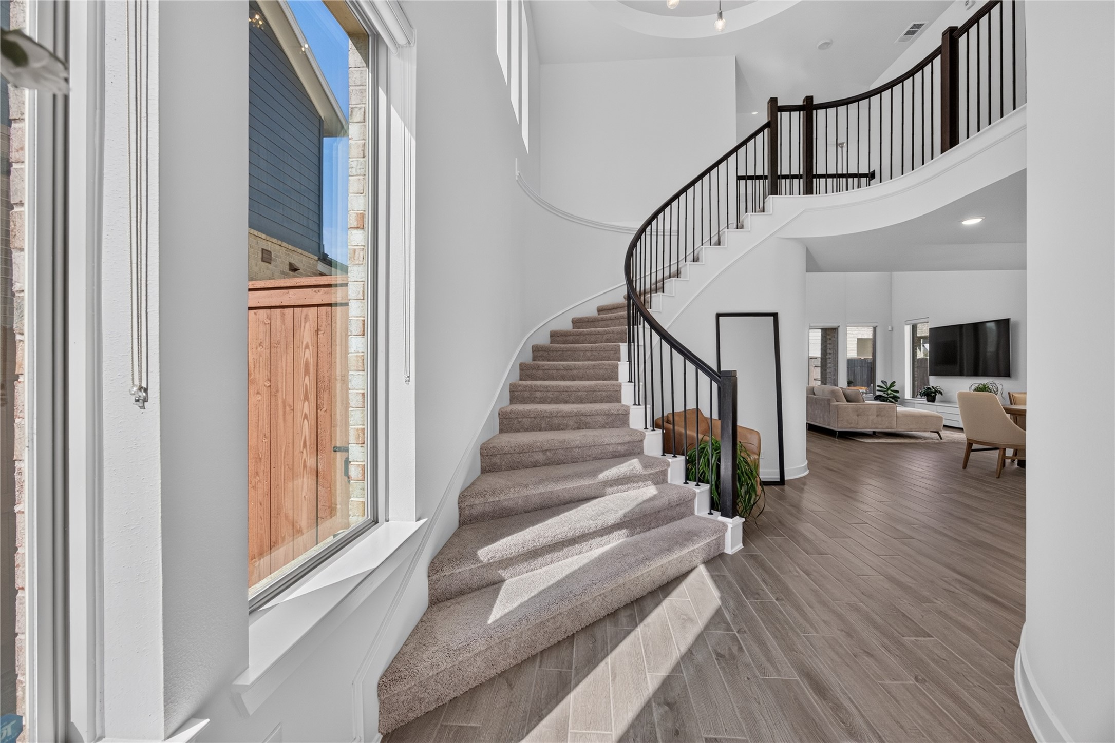 The foyer makes a memorable entrance with a sweeping curved staircase, dark handrail and iron balusters. Tall windows illuminate the stairway, while the soaring ceiling emphasizes the homes vertical space. Wood flooring continues toward the main living areas, creating visual continuity throughout the first floor.