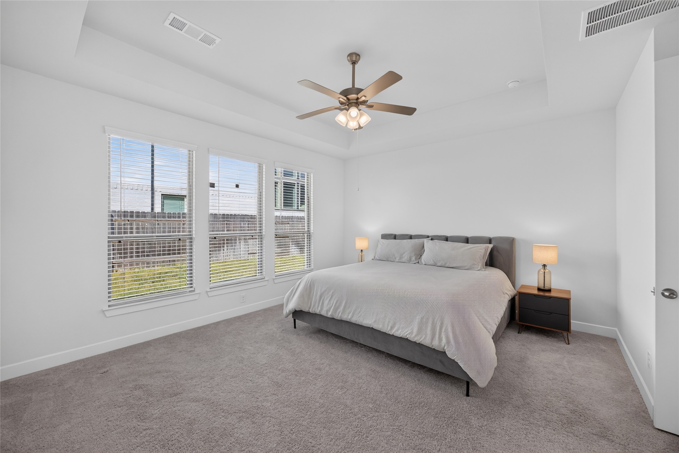 The first-floor primary bedroom offers a private retreat with a tray ceiling, ceiling fan and a broad bank of windows overlooking the backyard. Neutral walls and carpeting provide a versatile foundation for a variety of furnishings. The room offers space for a substantial bed and bedside pieces.