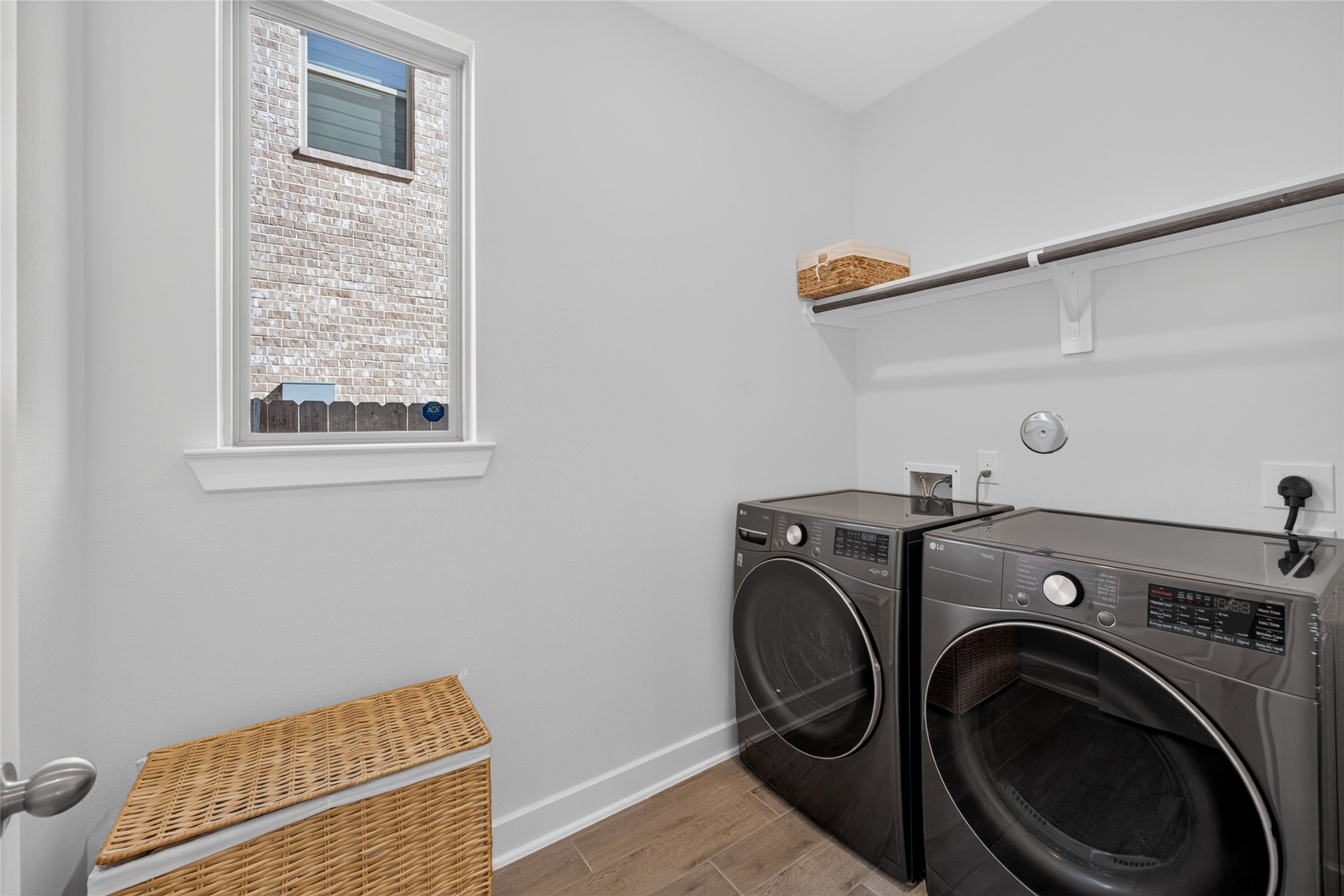 The dedicated laundry room provides space for side-by-side appliances and features a window that brings in natural light. An overhead shelf offers storage for laundry supplies, with a hanging rod below for air-drying or organizing clothing. The separate room keeps laundry tasks contained away from the main living spaces.
