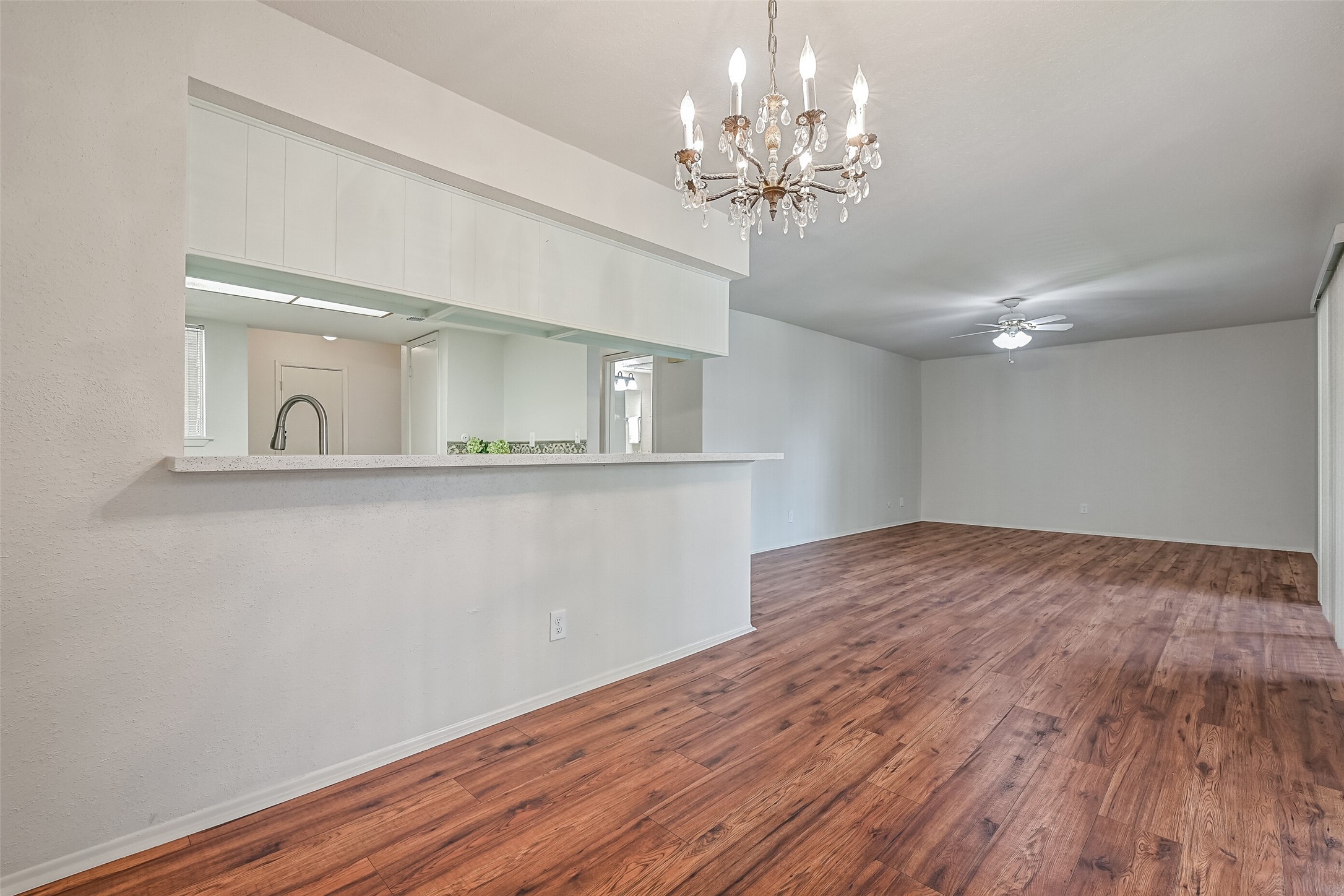 From the dining area, a wide pass-through opens to the kitchen, topped with a speckled countertop that doubles as a breakfast bar. The decorative chandelier adds character, while the open sightlines connect the dining space to the generously sized living room beyond.
