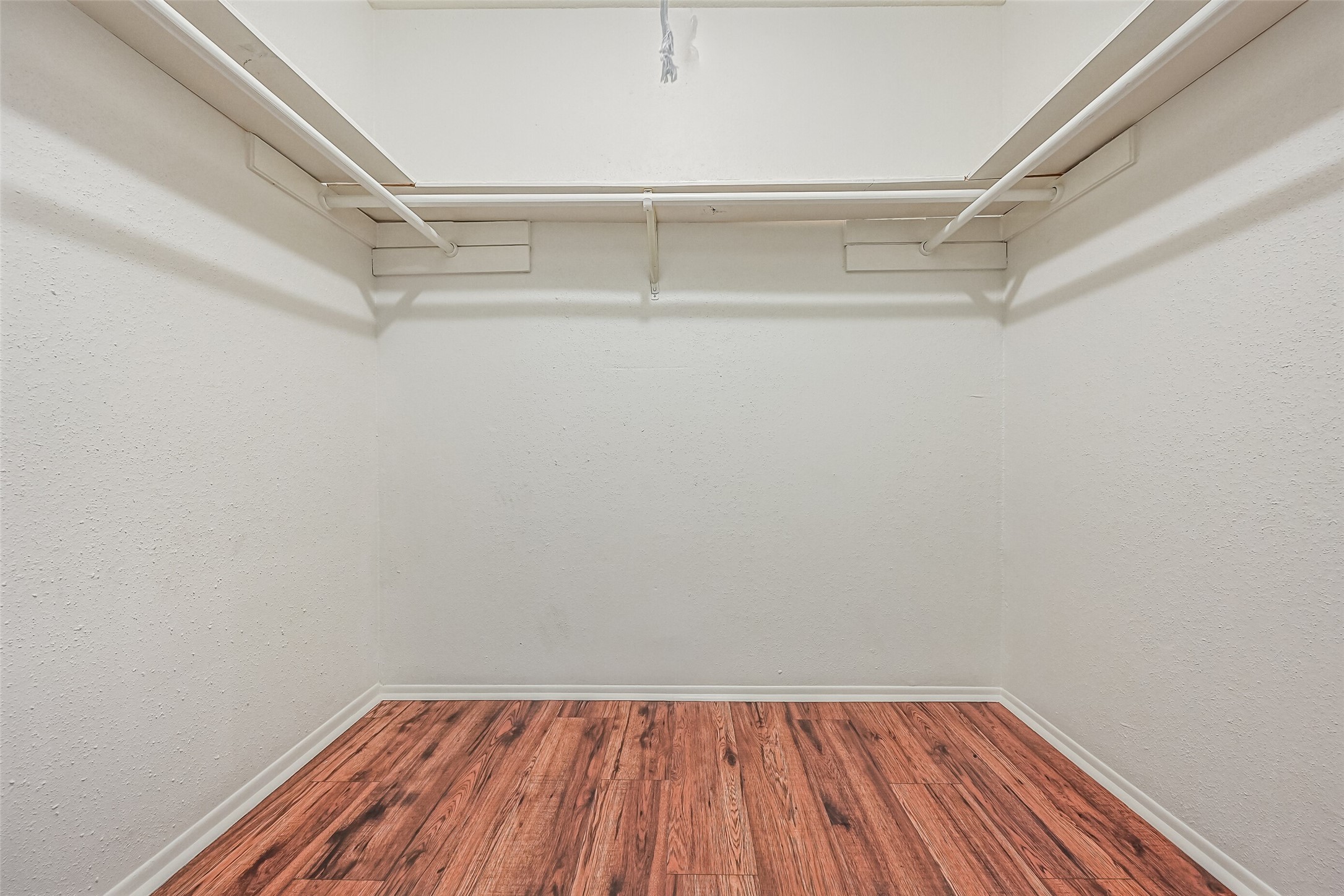 A generously sized walk-in closet provides excellent storage space in the primary suite! Hanging rods along both sides & the back wall offer plenty of room to organize clothing, while the wood-look flooring continues into the closet. There's also ample open floor space for additional storage solutions.