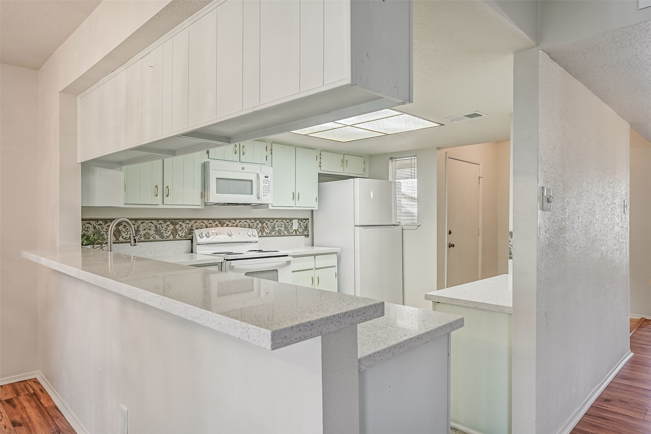 The spacious kitchen features an abundance of white cabinetry, speckled countertops & a decorative patterned backsplash. A wraparound breakfast bar provides additional counter space while opening to the dining area. White appliances & a large overhead light panel complete this functional space. The spacious kitchen features an abundance of white cabinetry, speckled countertops & a decorative patterned backsplash. A wraparound breakfast bar provides additional counter space while opening to the dining area. White appliances & a large overhead light panel complete this functional space.