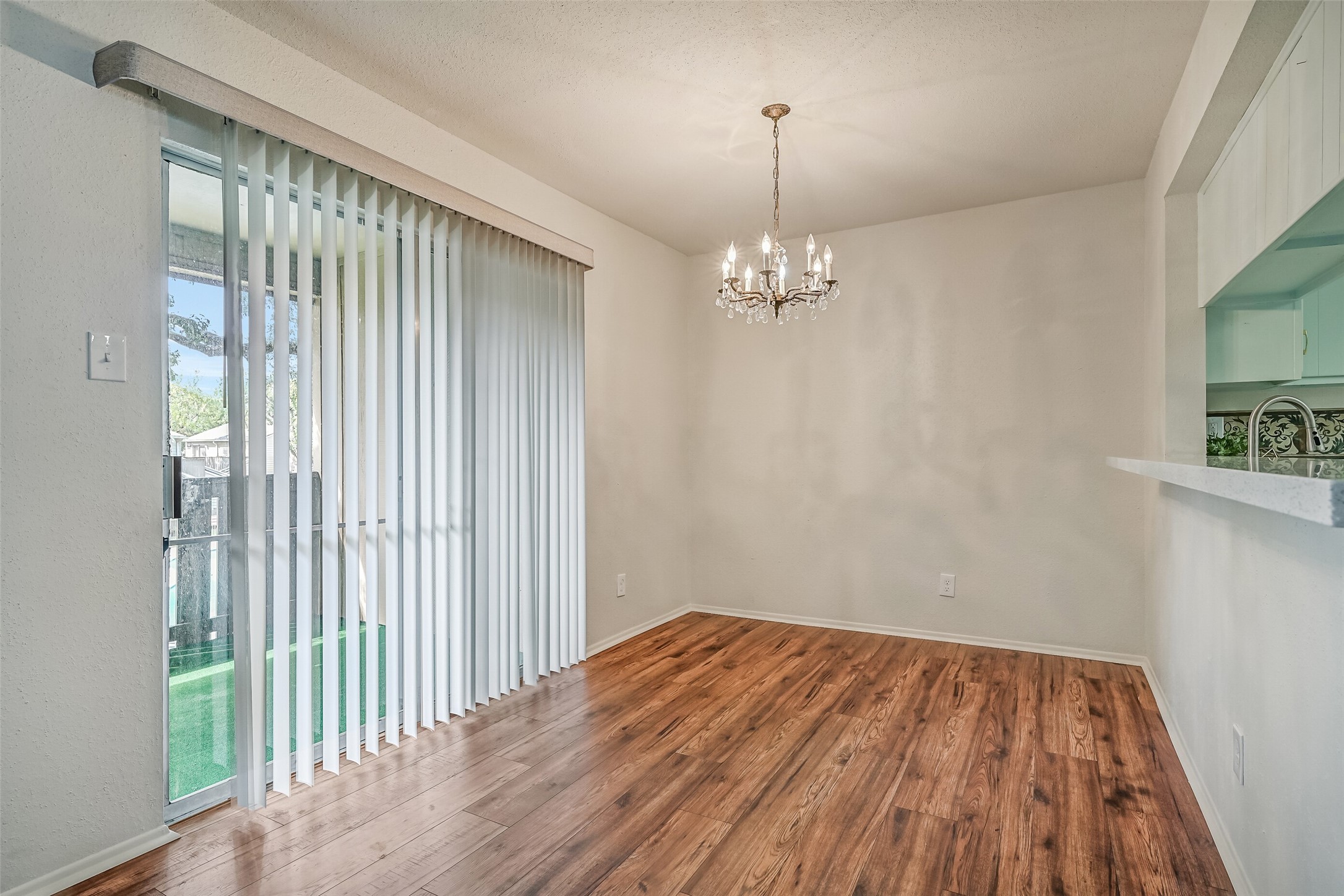 The dedicated dining area features a decorative chandelier, wood-look flooring & sliding glass doors leading directly to the covered balcony. Positioned beside the kitchen's breakfast bar, this inviting space offers room for a dining table while maintaining an open connection to the living room.