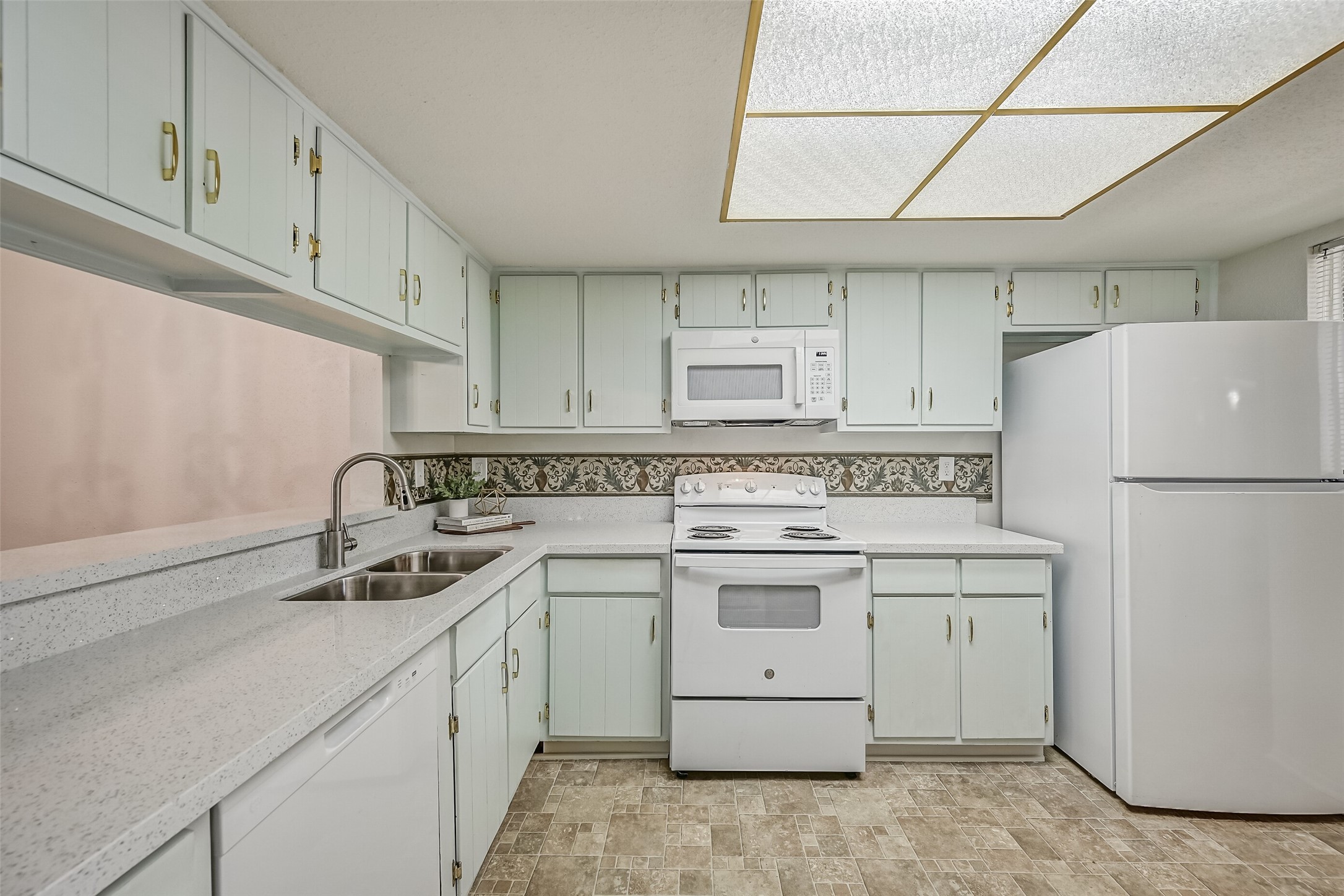 Another kitchen view showcases the extensive upper & lower cabinetry, white appliances & generous countertop space. Features include an electric range, built-in microwave, dishwasher, refrigerator & double-basin stainless steel sink with a gooseneck faucet. A decorative backsplash adds character.