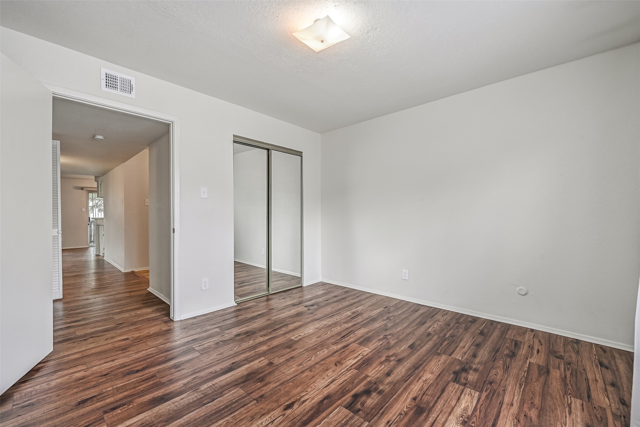 This secondary bedroom offers attractive wood-look flooring, neutral walls & a mirrored sliding-door closet that reflects light throughout the space. With room for bedroom furnishings and a versatile layout, this space could also serve as a home office or guest room.