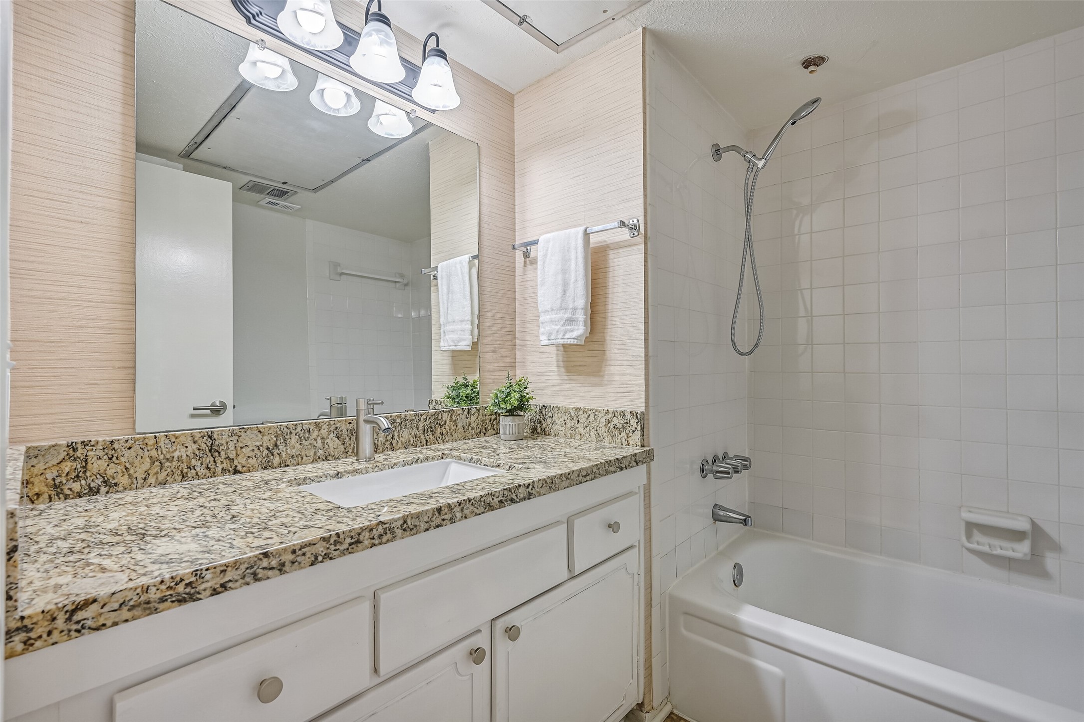 The adjoining full bathroom features a granite countertop with matching backsplash, undermount sink, updated faucet & contemporary vanity lighting. A large wall mirror adds to the open feel, while the white tiled tub/shower combination includes a handheld showerhead for added functionality.