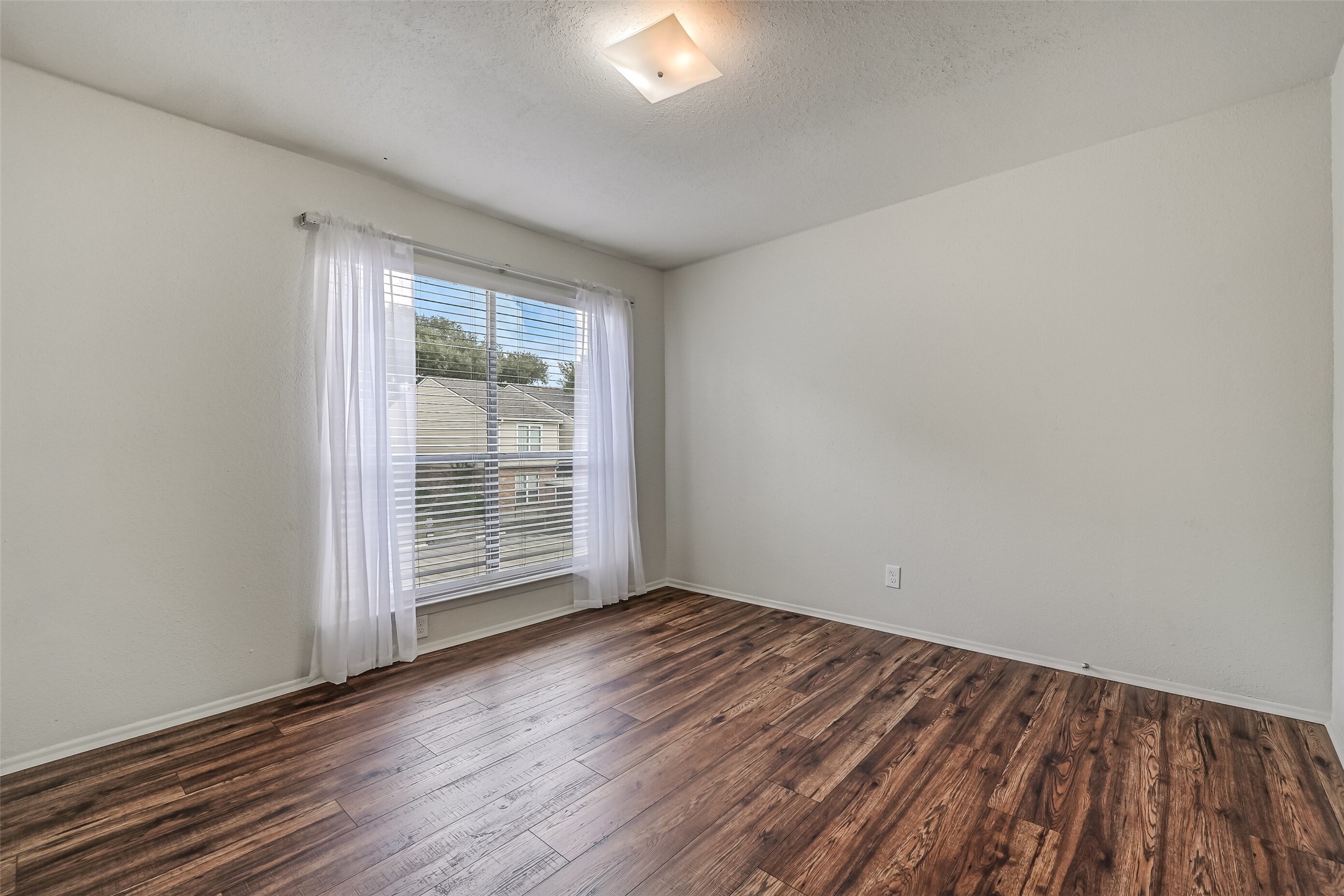 Natural light fills this inviting secondary bedroom through a large window with blinds & sheer curtains. The wood-look flooring continues into this room, complementing the neutral paint and providing a clean backdrop for your furnishings. A comfortable space to make your own!