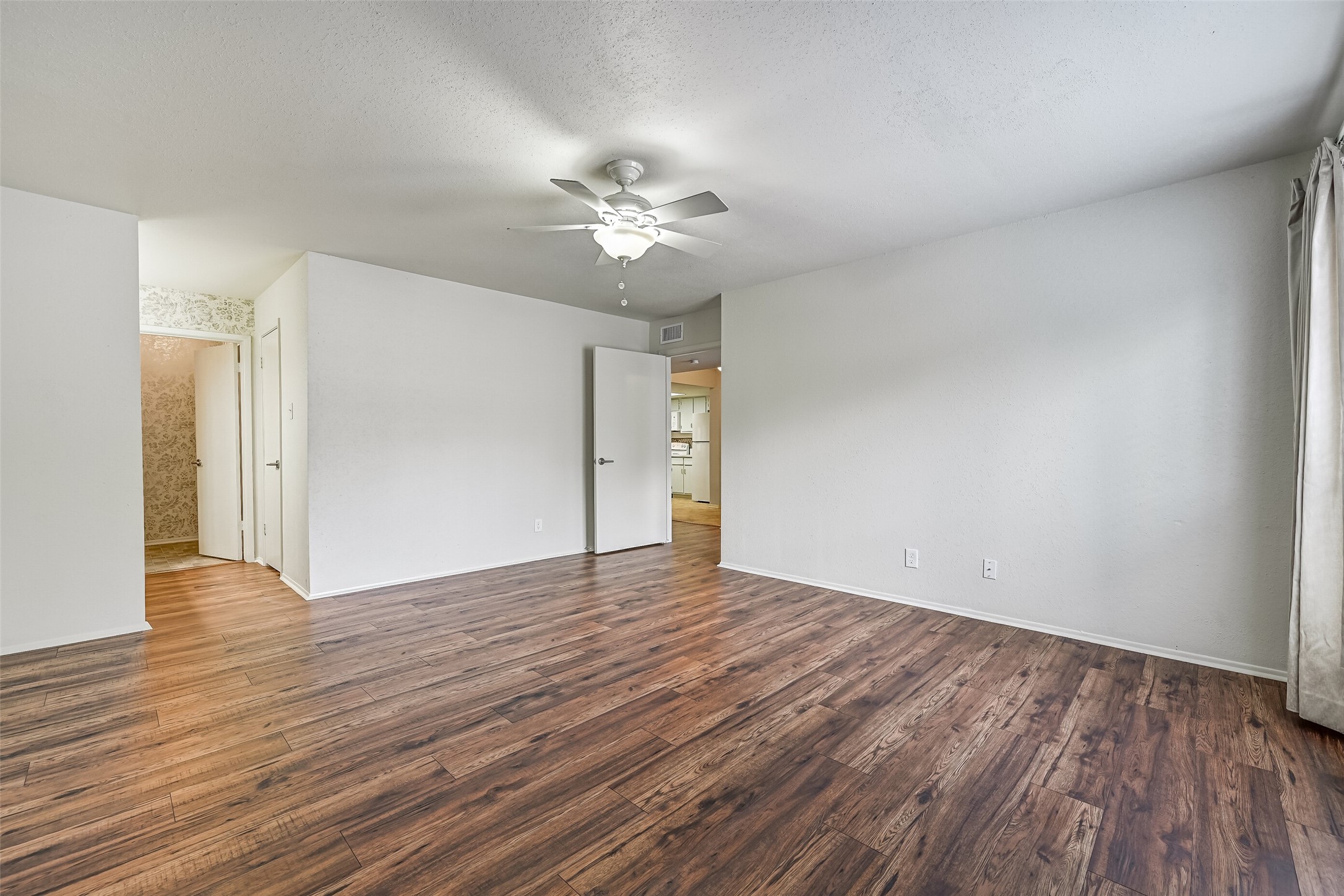 The spacious primary bedroom offers plenty of room for a king-sized bed & additional furnishings, with attractive wood-look flooring, neutral walls & a lighted ceiling fan. The generous floor plan includes access to a separate vanity area & bathroom, creating a comfortable primary suite.