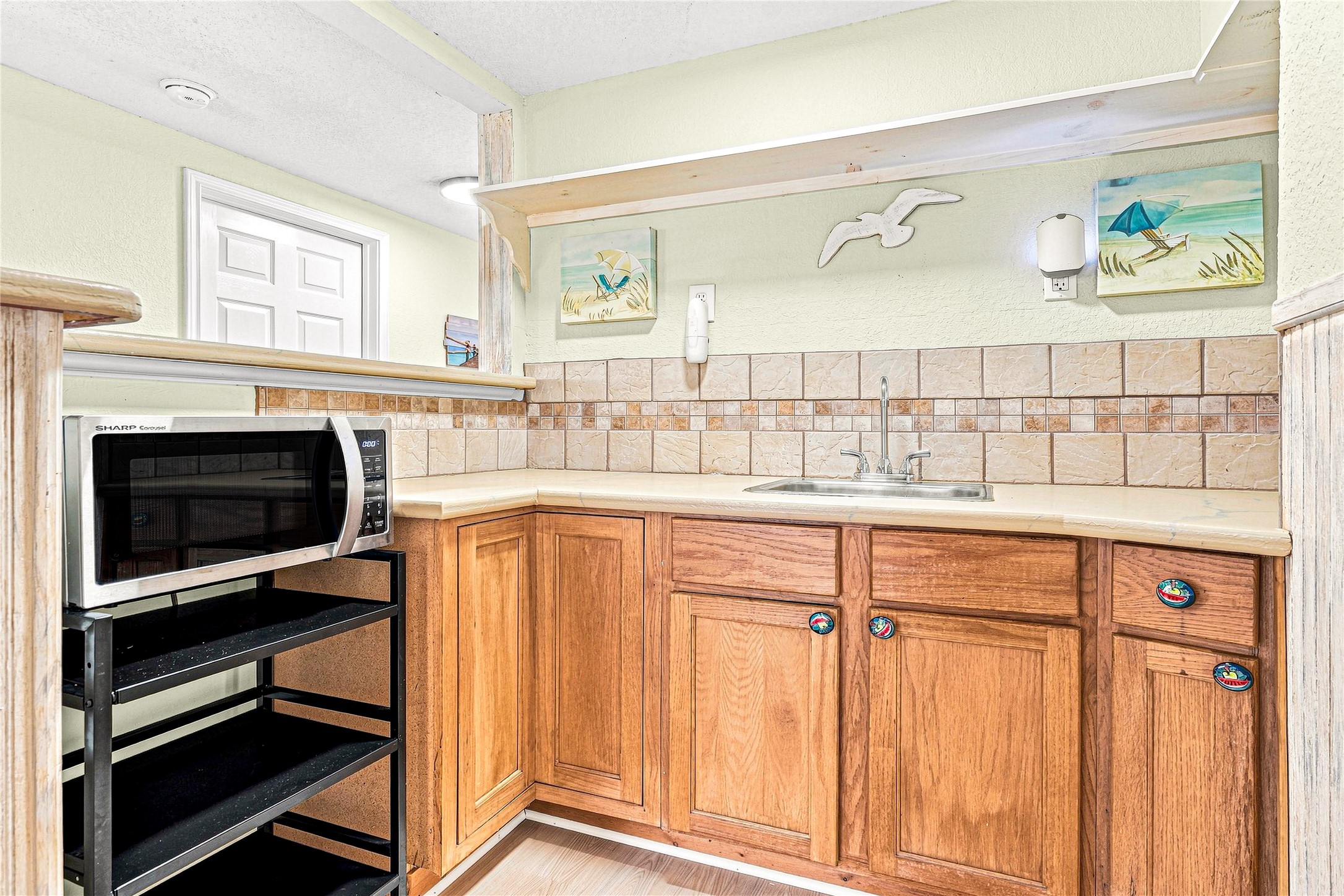 Charming kitchenette with warm wood cabinets, decorative tile backsplash, and convenient countertop space, perfect for light meal prep or entertaining.