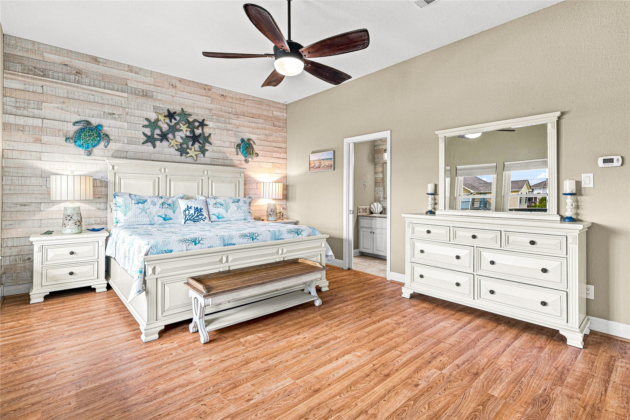 Spacious bedroom featuring a coastal theme with a king-size bed, stylish wood accent wall, and elegant white furniture.