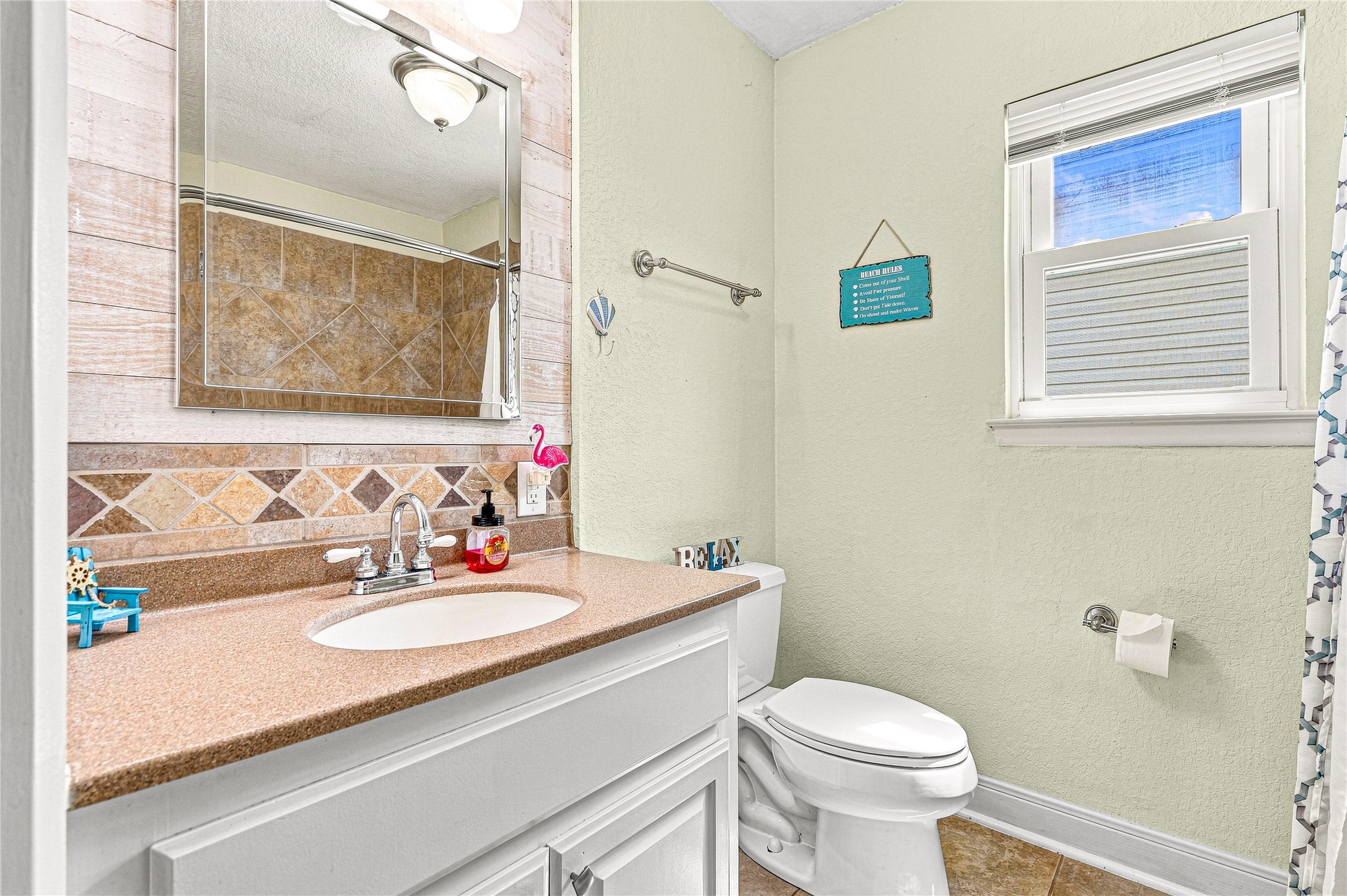 Charming bathroom with a warm, neutral palette features a sleek countertop, stylish tiled backsplash, and a bright window for natural light.