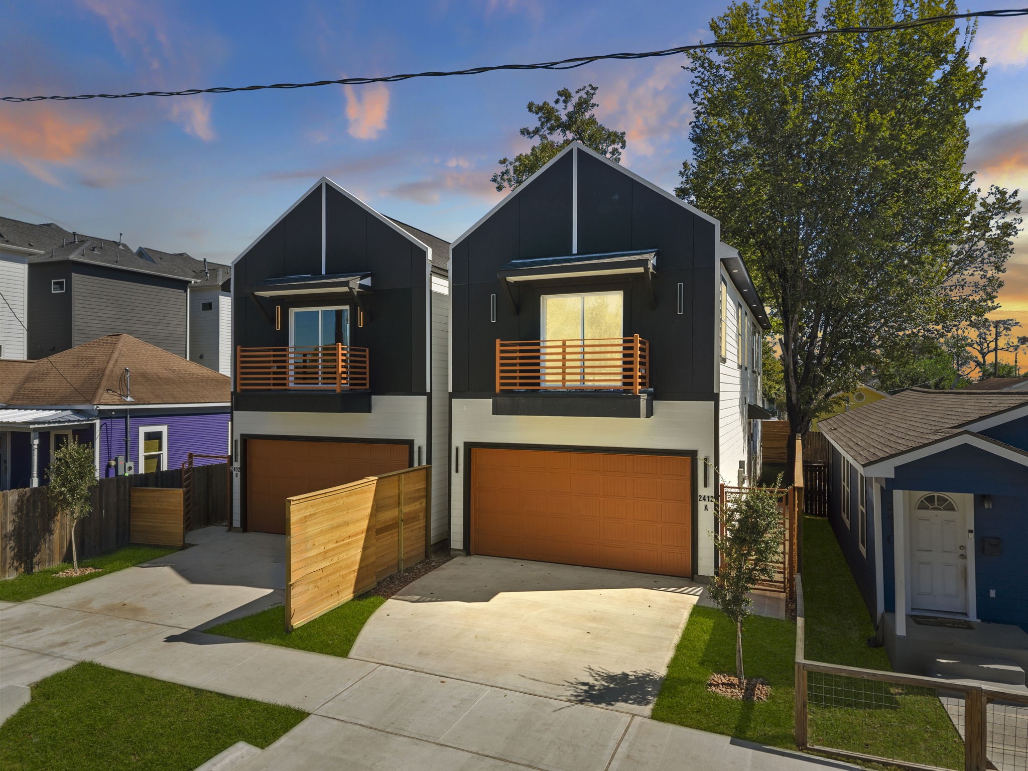 This striking two-story home features sharp gabled architecture and sleek modern paneling. Private upper balconies extend the living space outdoors, while an expansive concrete driveway and neatly landscaped yard provide generous off-street parking and excellent functional footprint.