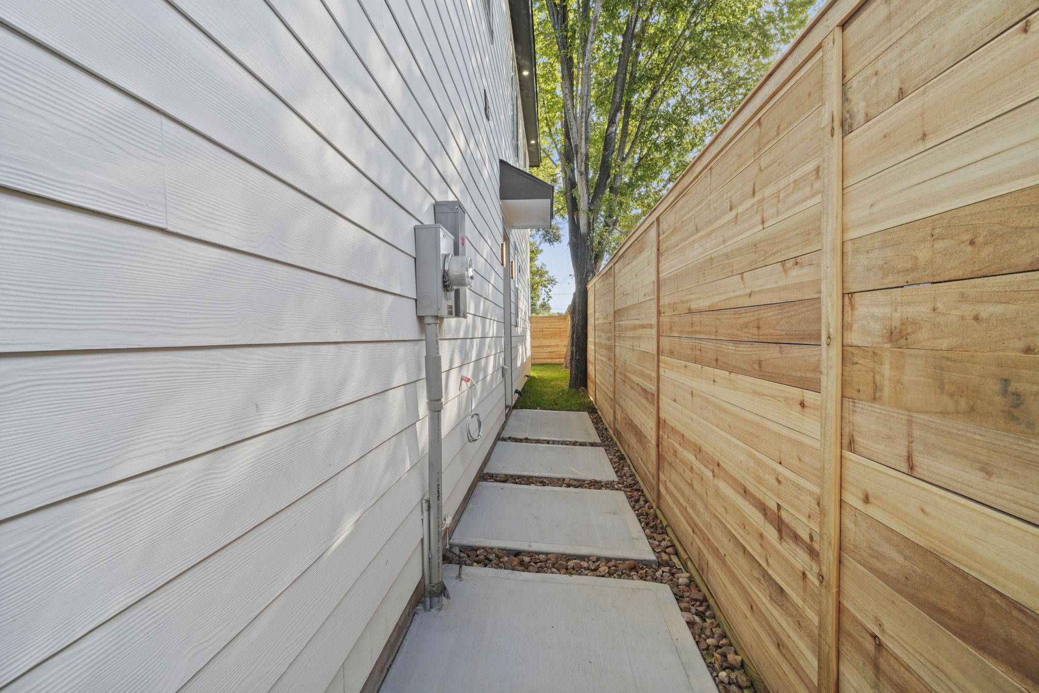 This private side pathway features modern horizontal wood fencing paired with clean concrete paver walkways framed by decorative gravel.
