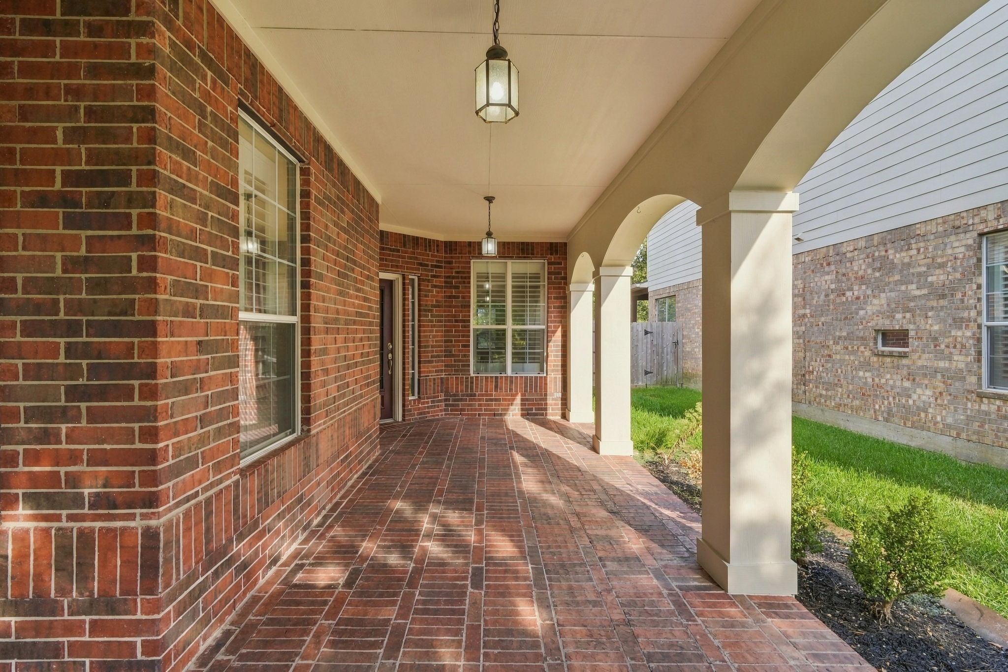 Step into relaxation on this expansive covered porch featuring graceful architectural arches and classic brick flooring. Beautiful pendant lanterns illuminate the pathway, creating a warm retreat.