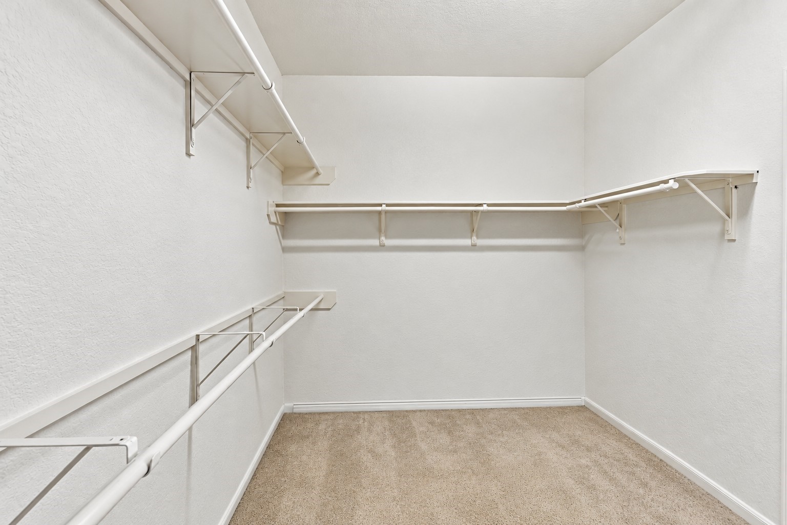 A spacious walk-in primary closet offering generous storage and organization space. Multiple hanging rods and built-in shelving extend along several walls, providing plenty of room for clothing, shoes, and accessories.