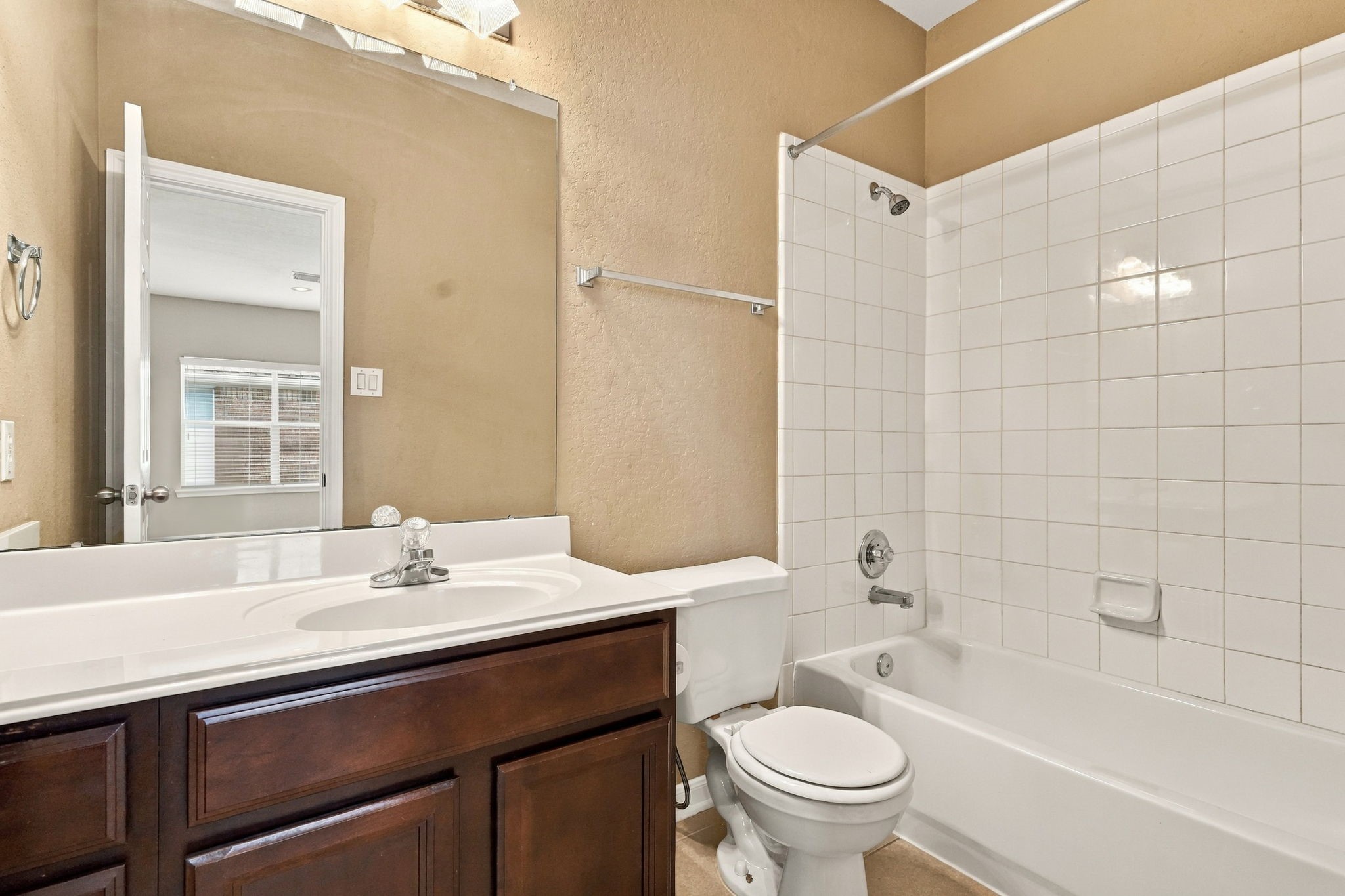 Offering a practical full-bath setup, this space incorporates a single sink vanity with lower storage, bright vanity overhead lighting, and a full-size soaking tub with shower fixtures.