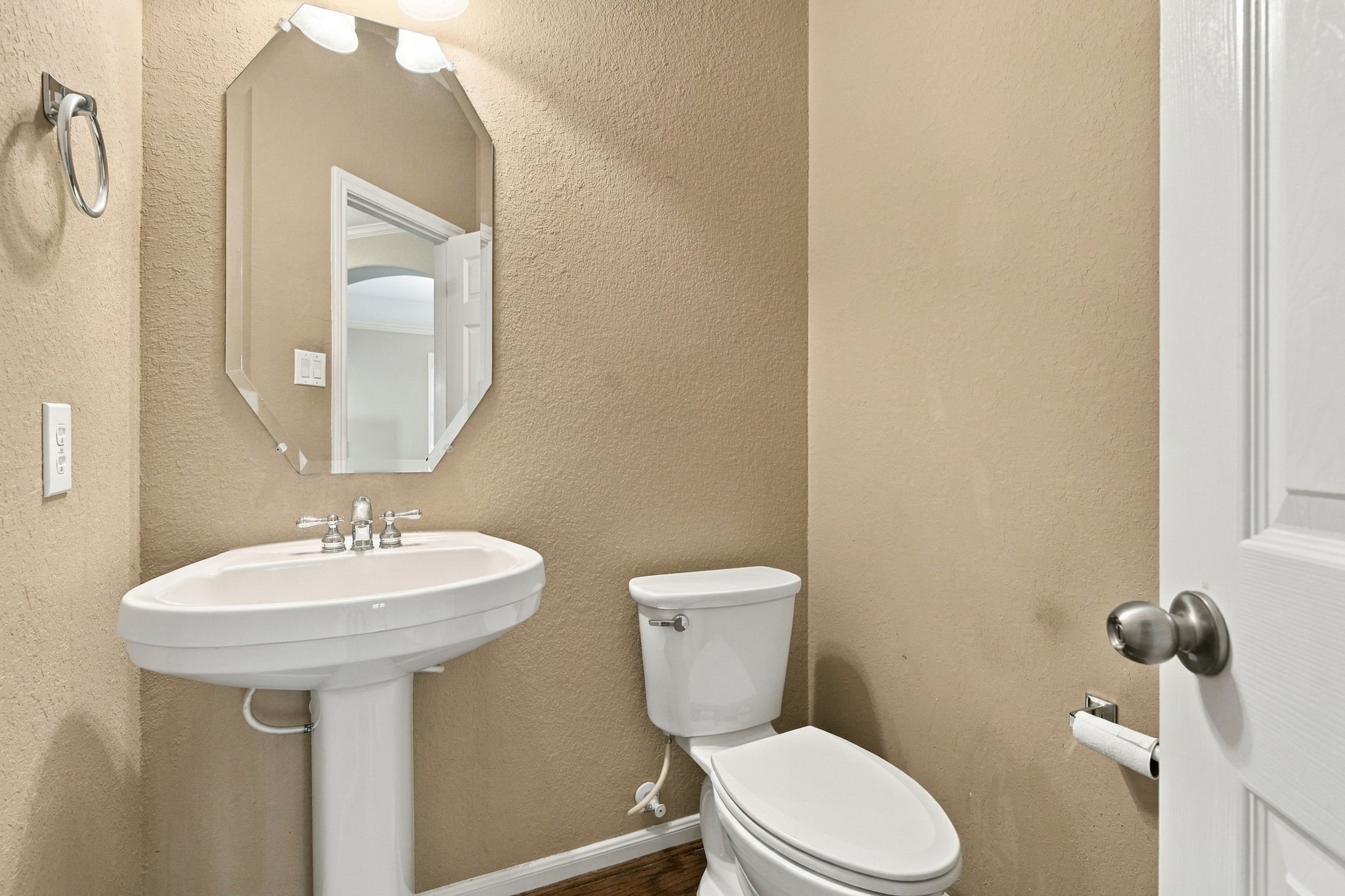 A clean and functional half bath featuring warm neutral walls, and crisp white trim. The space includes a pedestal sink.